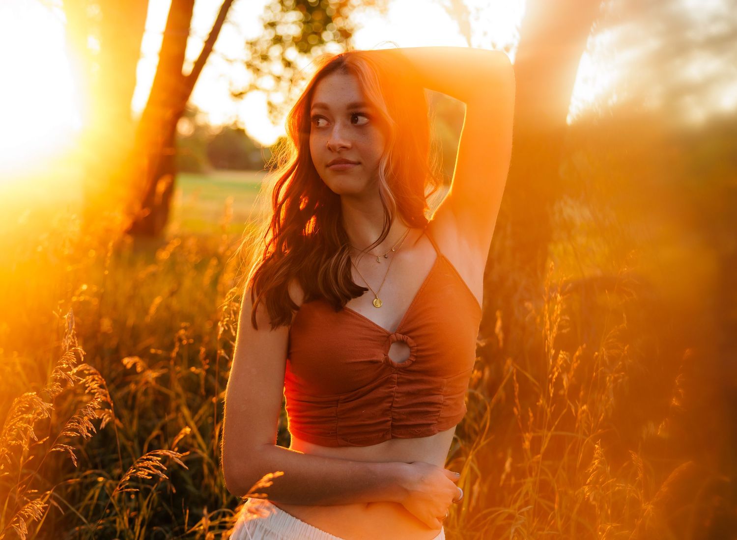 Young woman in rust crop top posing in tall grass during golden hour  for Parker CO Dreamy Senior photos