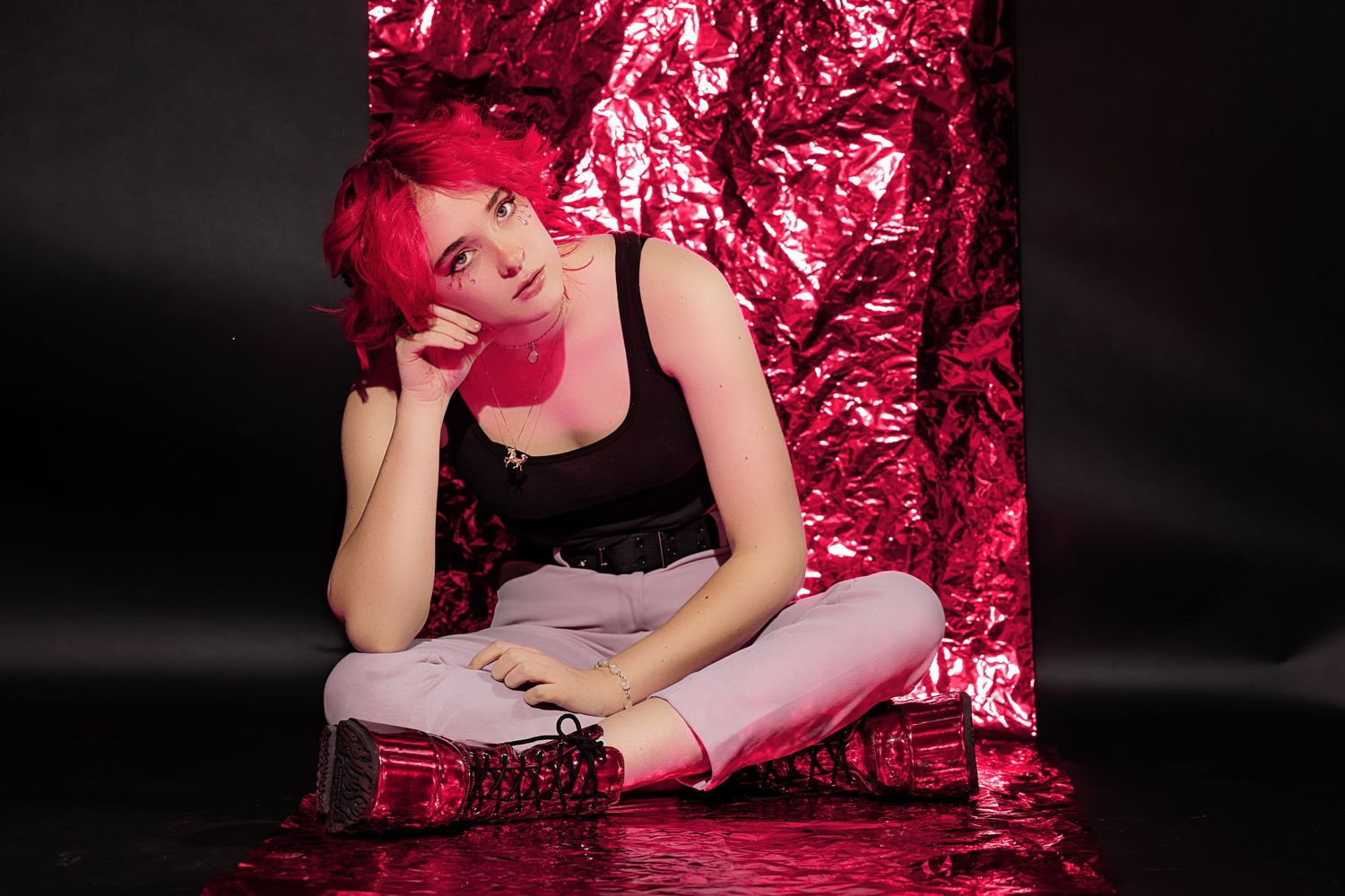 Colorado High School woman with pink hair sitting cross-legged against a shiny pink metallic background in a dark studio in Parker CO Studio
