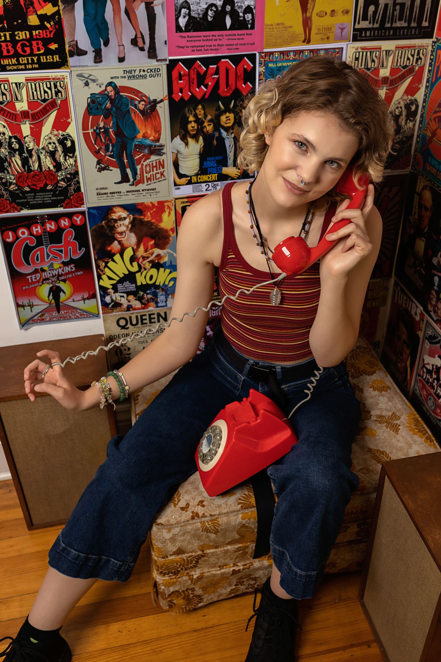 Teen holding red vintage rotary phone poses in front of classic rock music concert posters posing for senior photos Parker Colorado