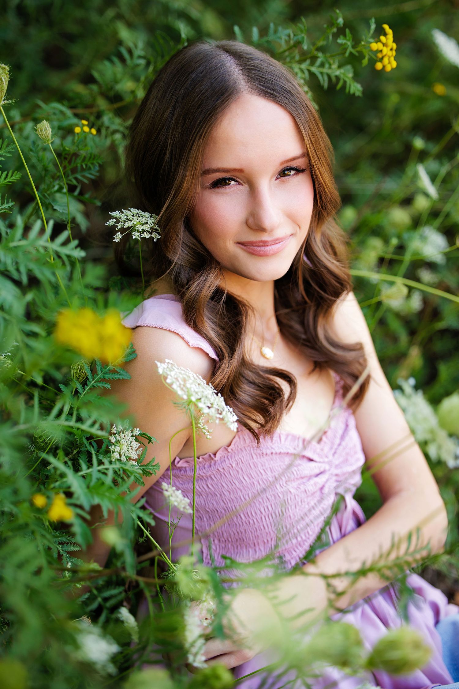 Young woman in lavender dress smiling among lush green foliage and wildflowers outdoors in Littleton Colorado