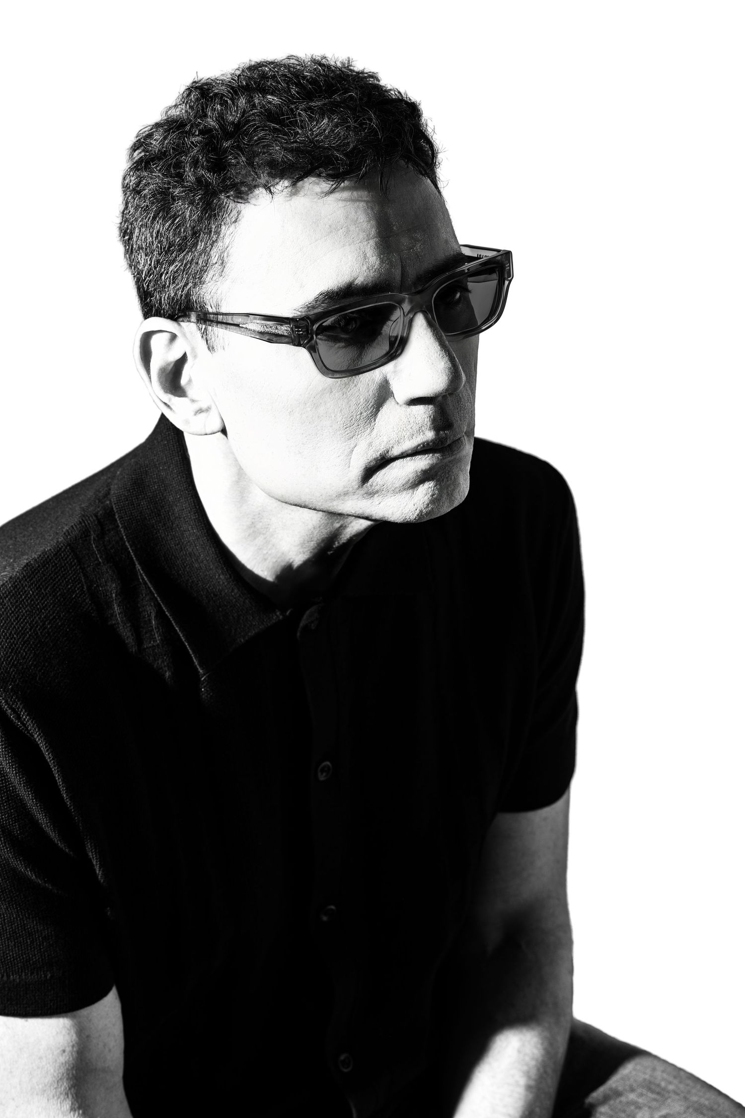 Black and white portrait of a man in a black polo shirt wearing sunglasses, looking to the side. Parker Colorado Poet Headshot