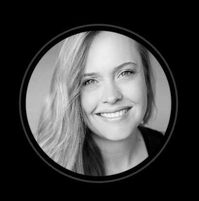 Black and white circular headshot of a smiling woman with long, wavy hair looking warmly at the camera.