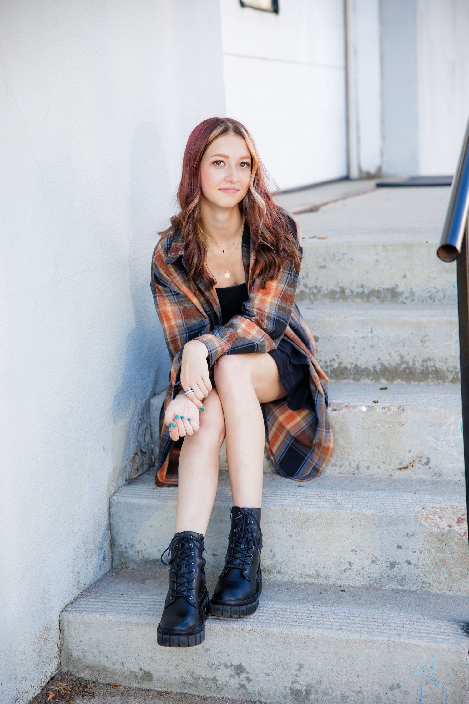 Young woman with auburn hair in plaid coat and black boots sitting on outdoor steps Urban Downtown Denver CO Senior photos