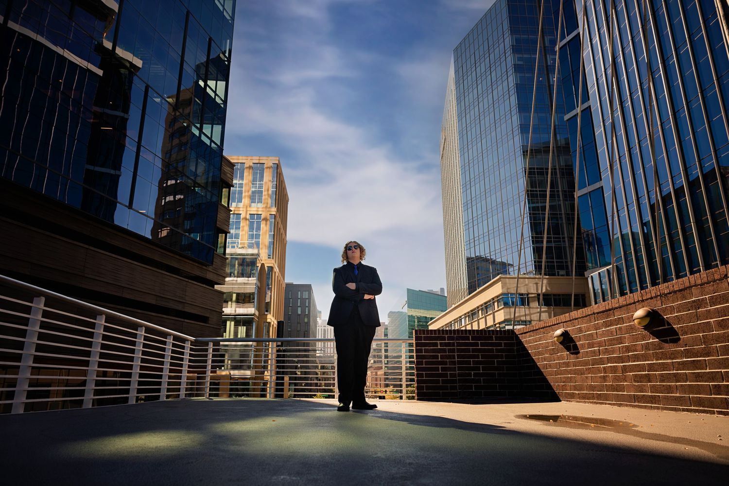 Business style senior on urban rooftop terrace surrounded by modern glass skyscrapers under blue sky in Downtown Denver