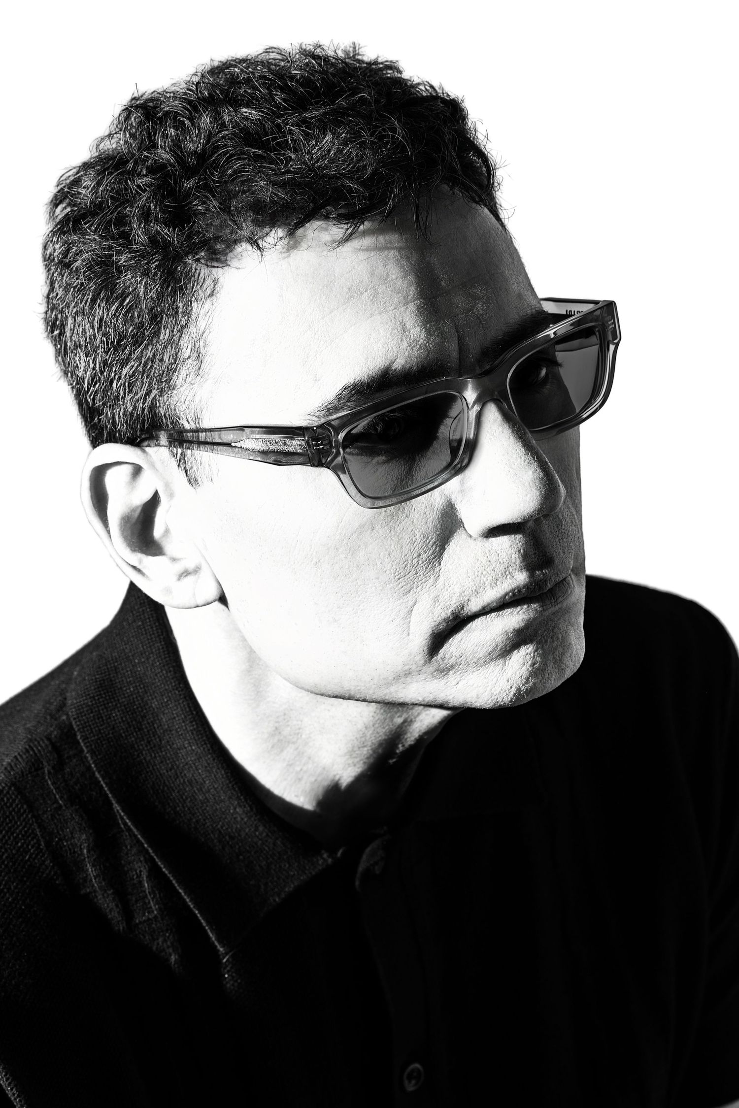 Black and white portrait of a man wearing dark sunglasses and a black shirt, gazing downward. Douglas Country Colorado Writer Headshot