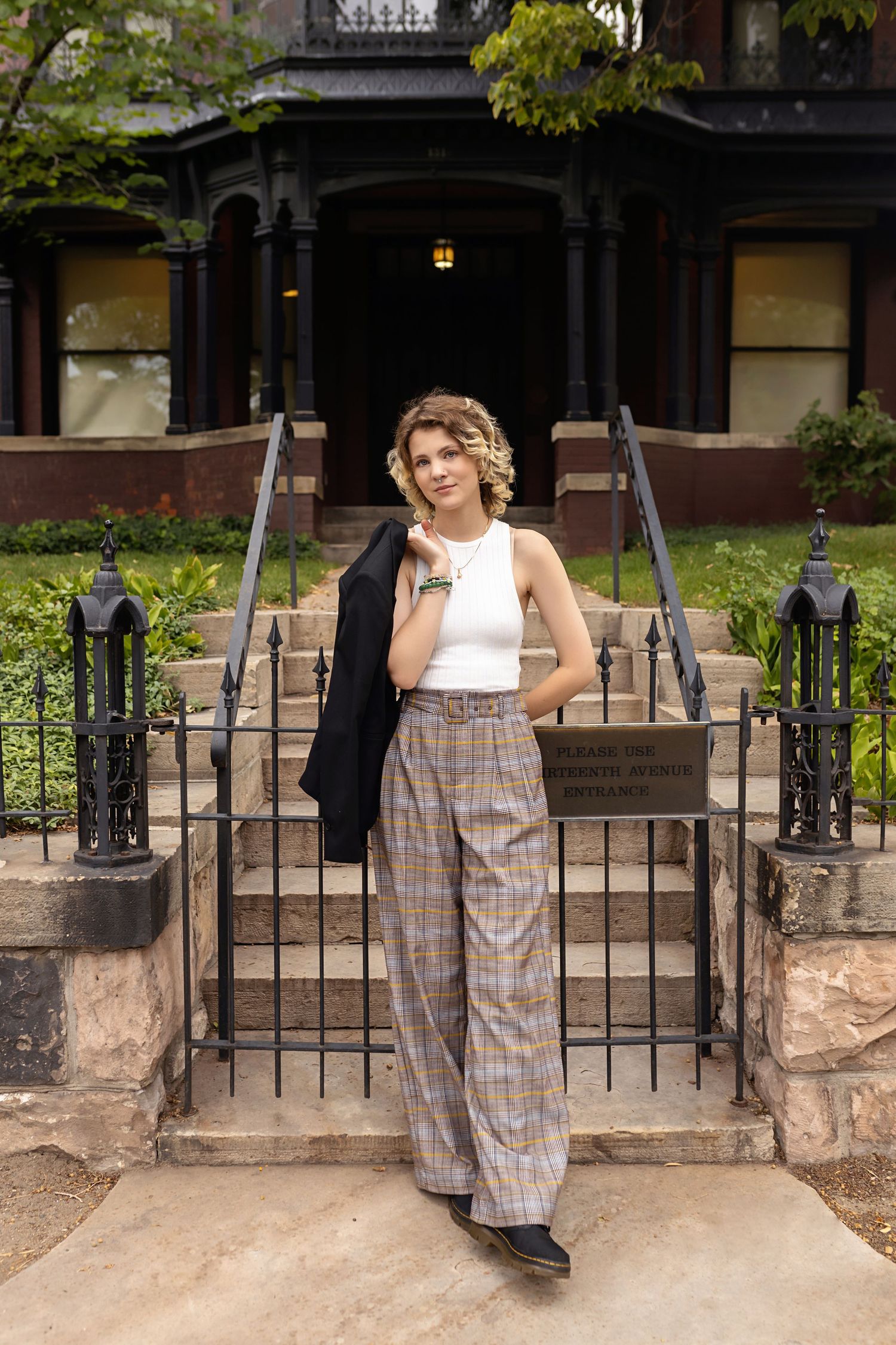 Elegant Parker Colorado LGBTQ friendly images teen in plaid wide-leg pants holds black blazer while standing at historic building entrance.