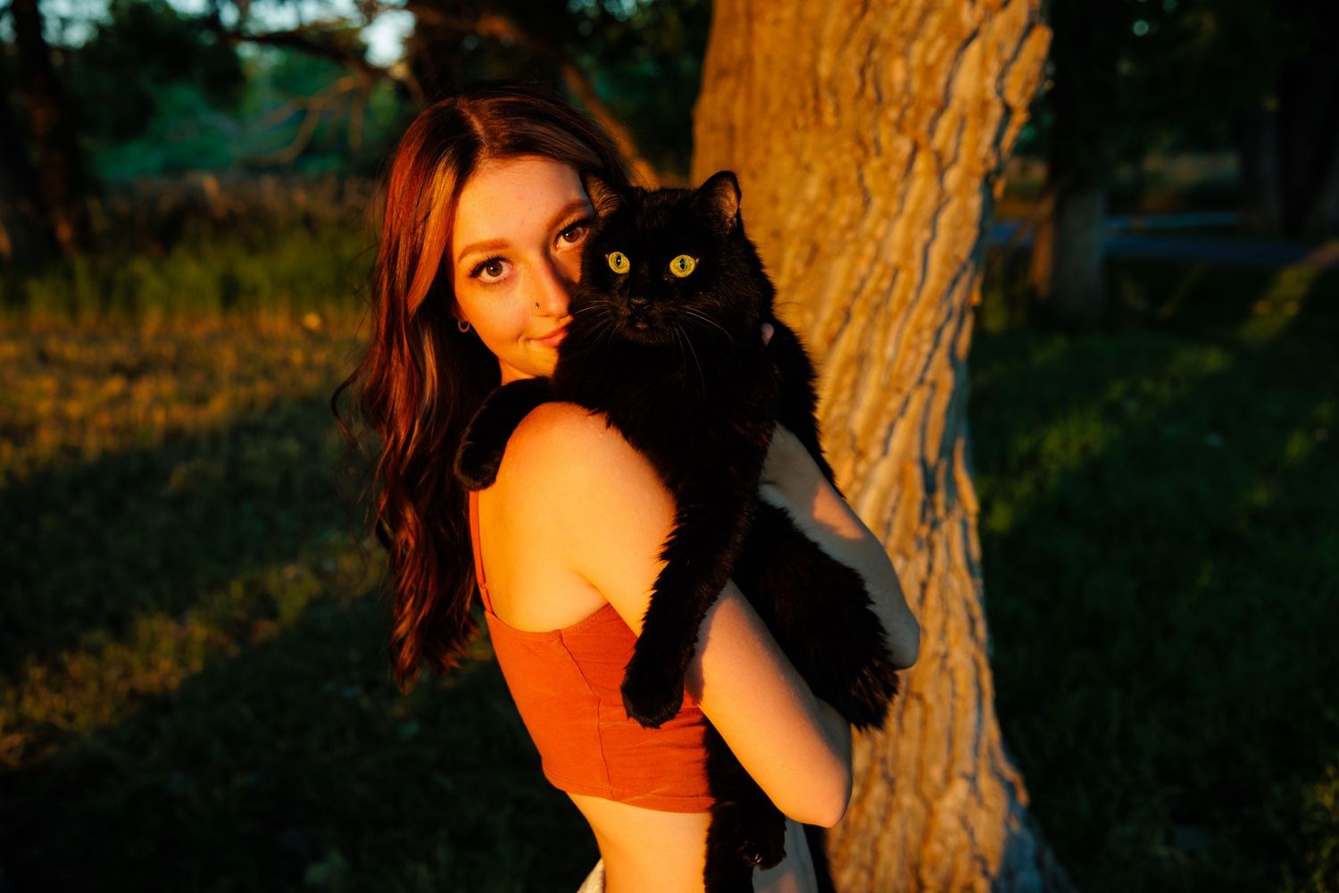 Young woman holding black cat near tree in golden sunset light  for Parker CO Senior photos