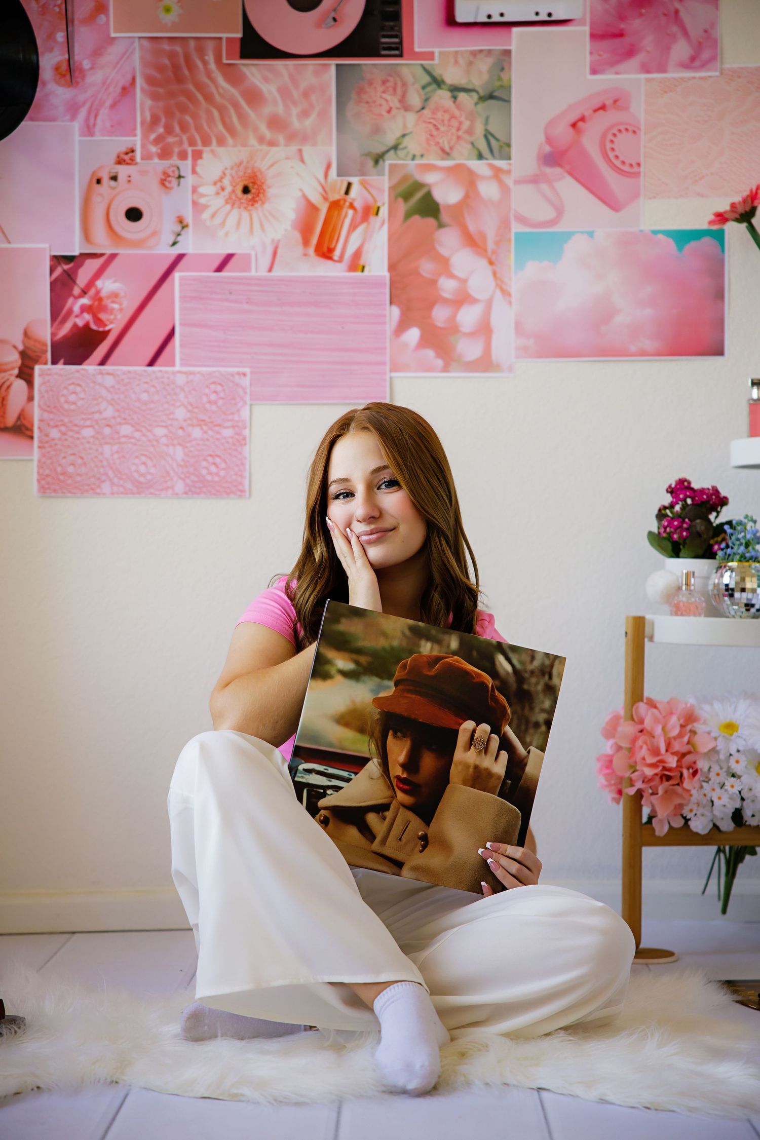 A teenage girl sits cross-legged holding a vinyl record album in a pink aesthetic room with a collage wall backdrop.