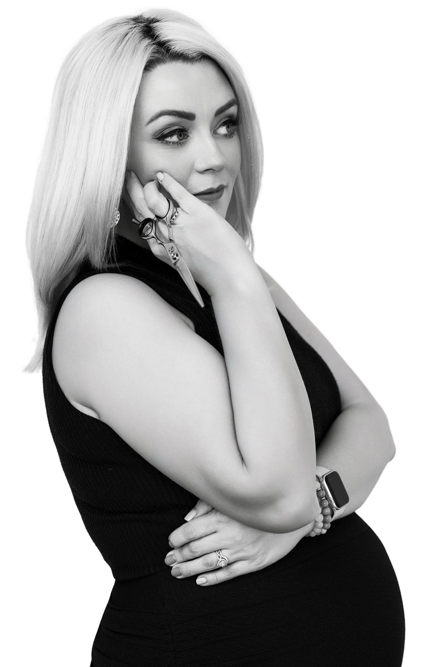 Black and white portrait of a blonde woman in a black dress, thoughtfully touching her face with ringed fingers. Parker Colorado Hairdresser