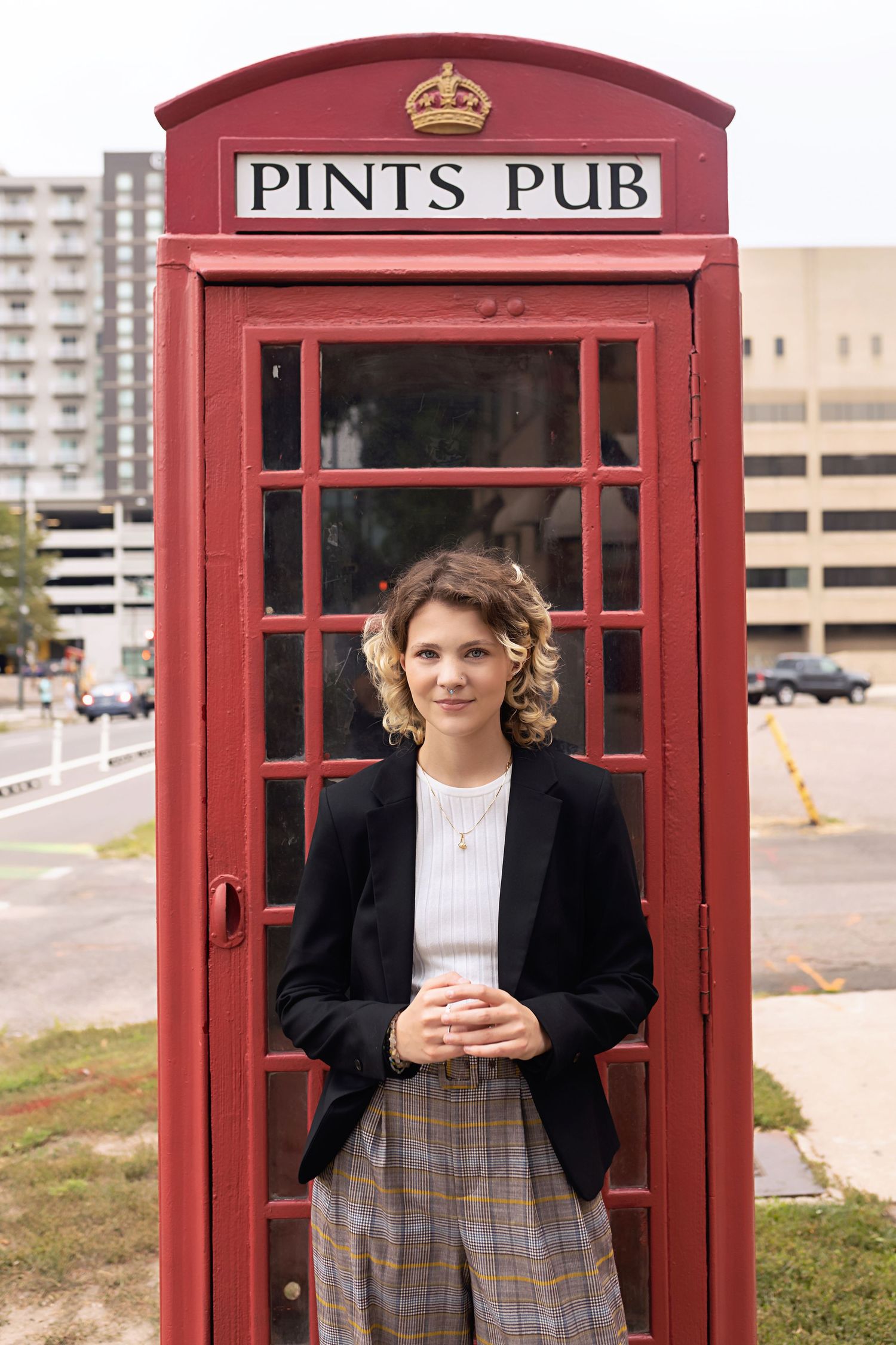 Person in black blazer stands smiling beside iconic red British phone box at Pints Pub. High School Senior Colorado