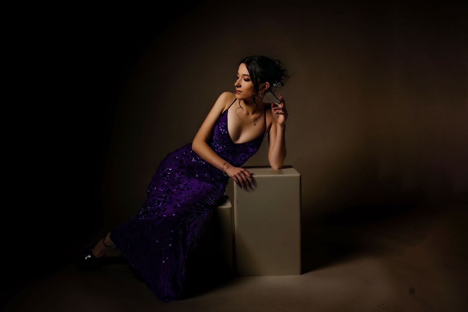 Woman in purple sequin gown poses elegantly on white cube in dramatic studio lighting In Parker Colorado Studio