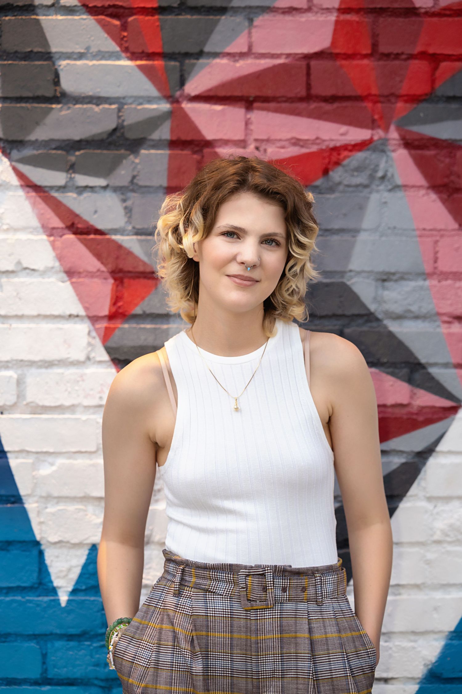 Androgynous high school senipr in white ribbed tank top and plaid pants posing before colorful graffiti wall. Parker Colorado Senior Picture