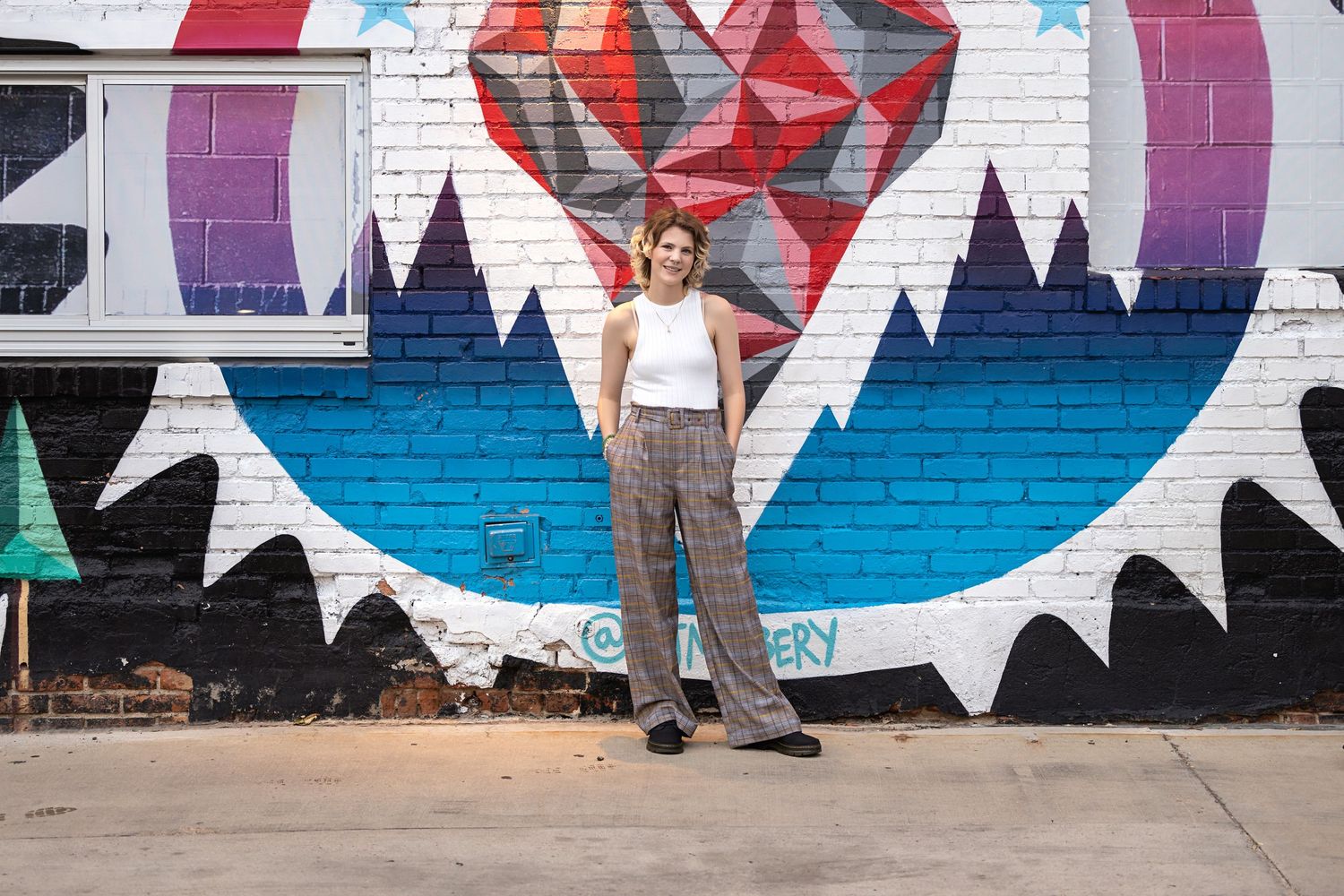 High School Senior in white tank top and plaid pants standing before vibrant heart street mural. Lonetree Colorado Senior Portrait