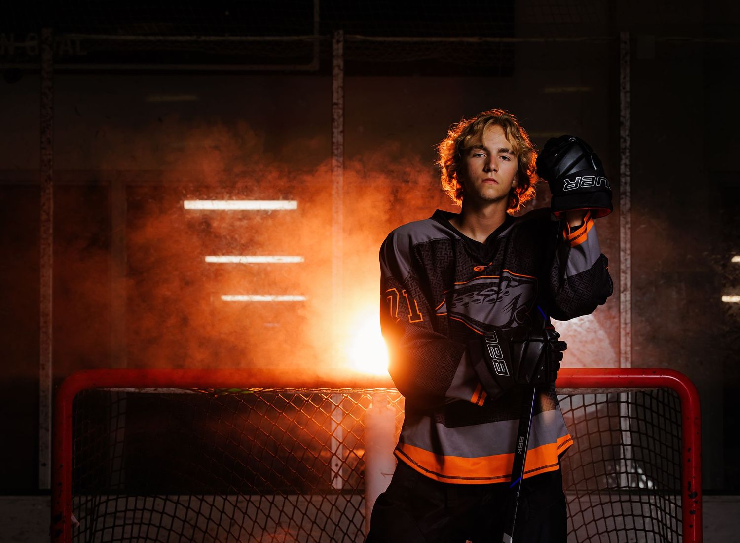 Young hockey player posing dramatically in front of net with orange smoke.