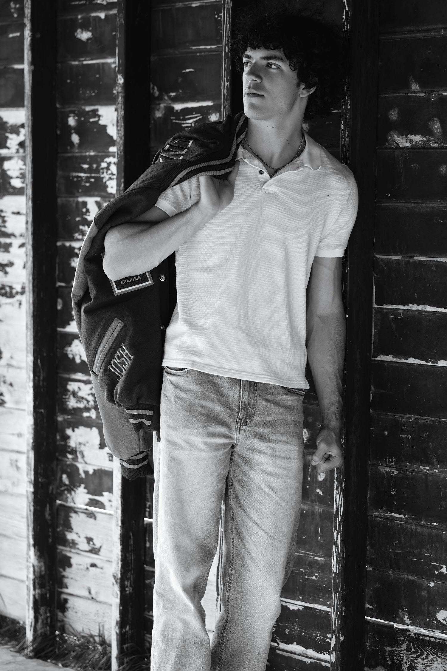 Black and white portrait of young man leaning against rustic wooden wall.