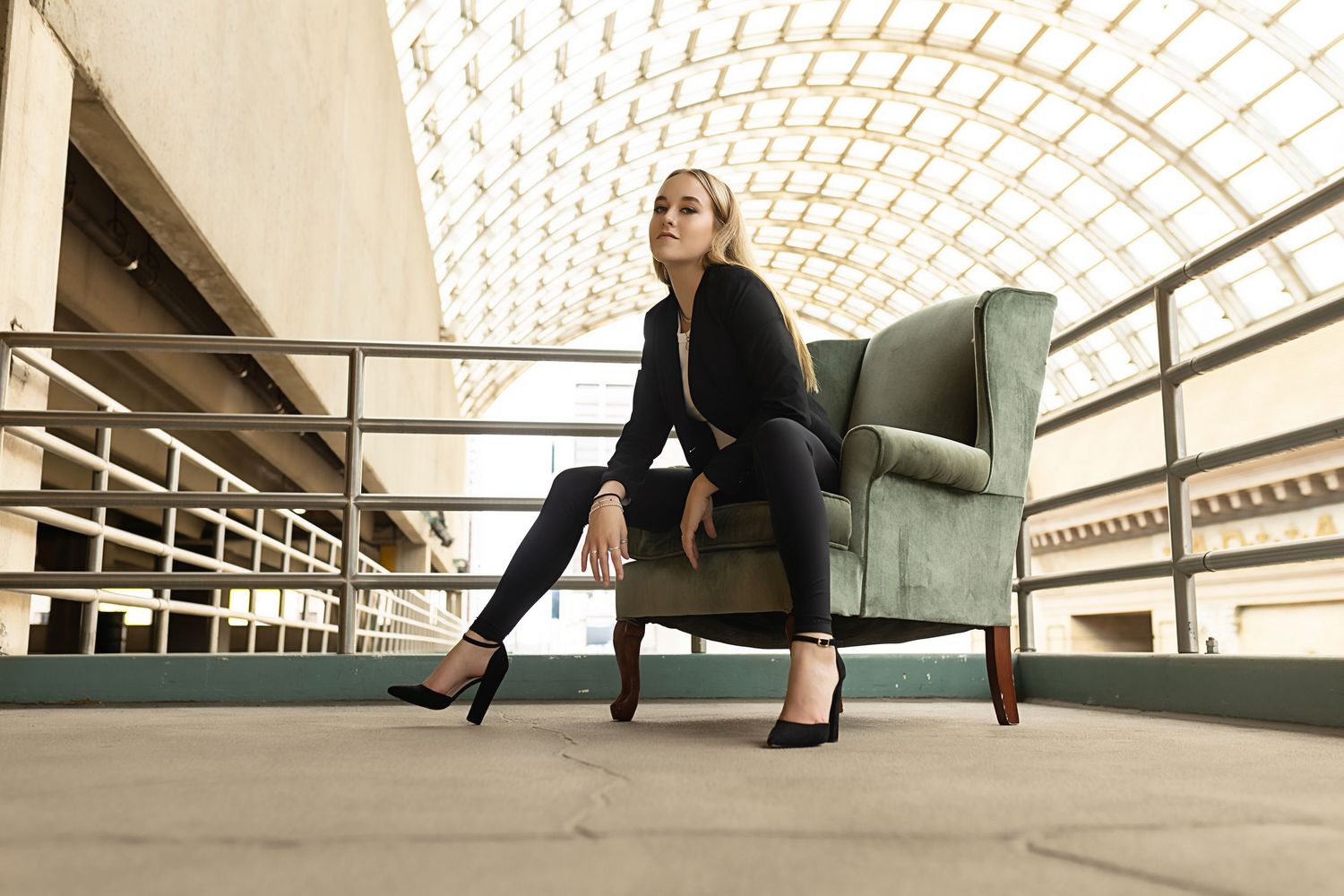 Woman in black outfit seated on green armchair in modern architectural space with geometric ceiling in Downtown Denver