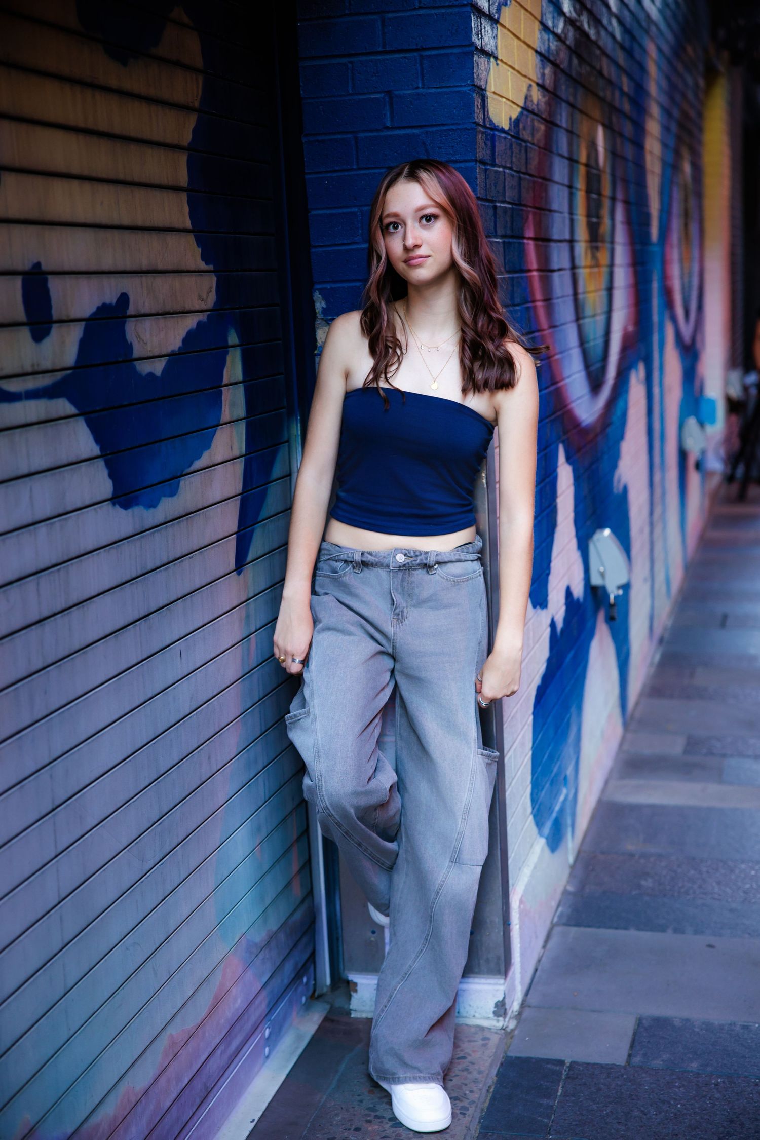 Teen girl in navy crop top and wide-leg jeans leaning against colorful graffiti wall for Parker Colorado Senior pictures