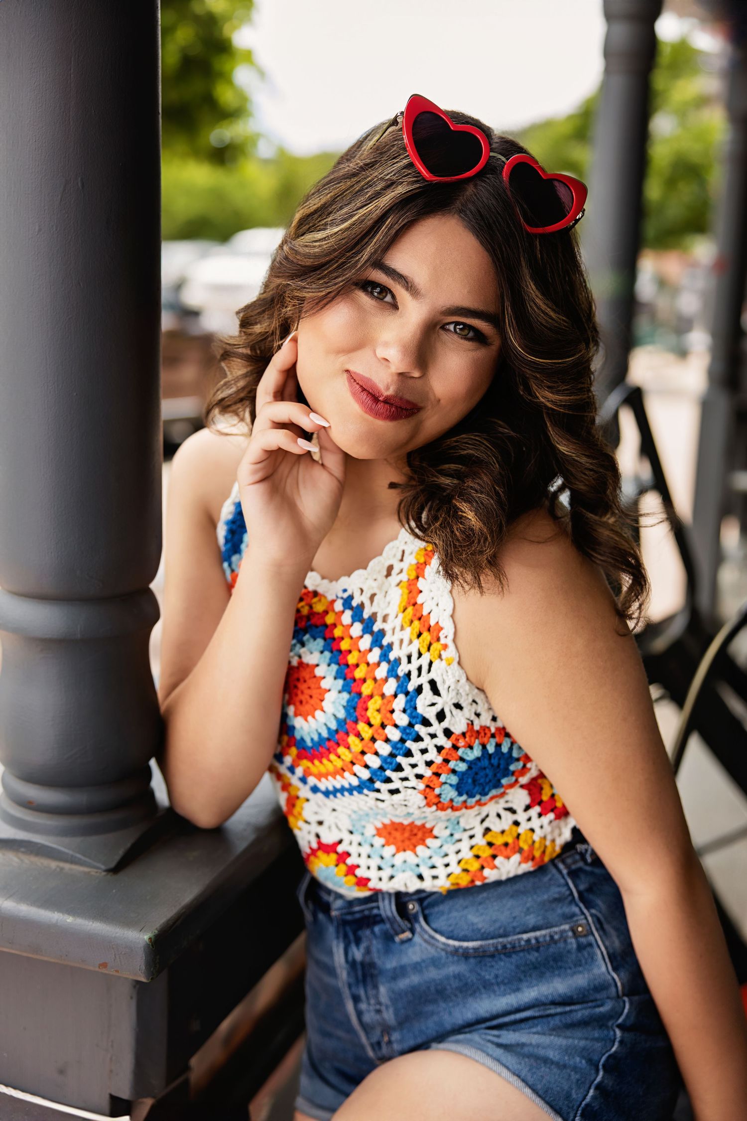 Pretty young woman in colorful crochet halter top with red heart sunglasses at outdoor venue for Paker High School Senior pictures