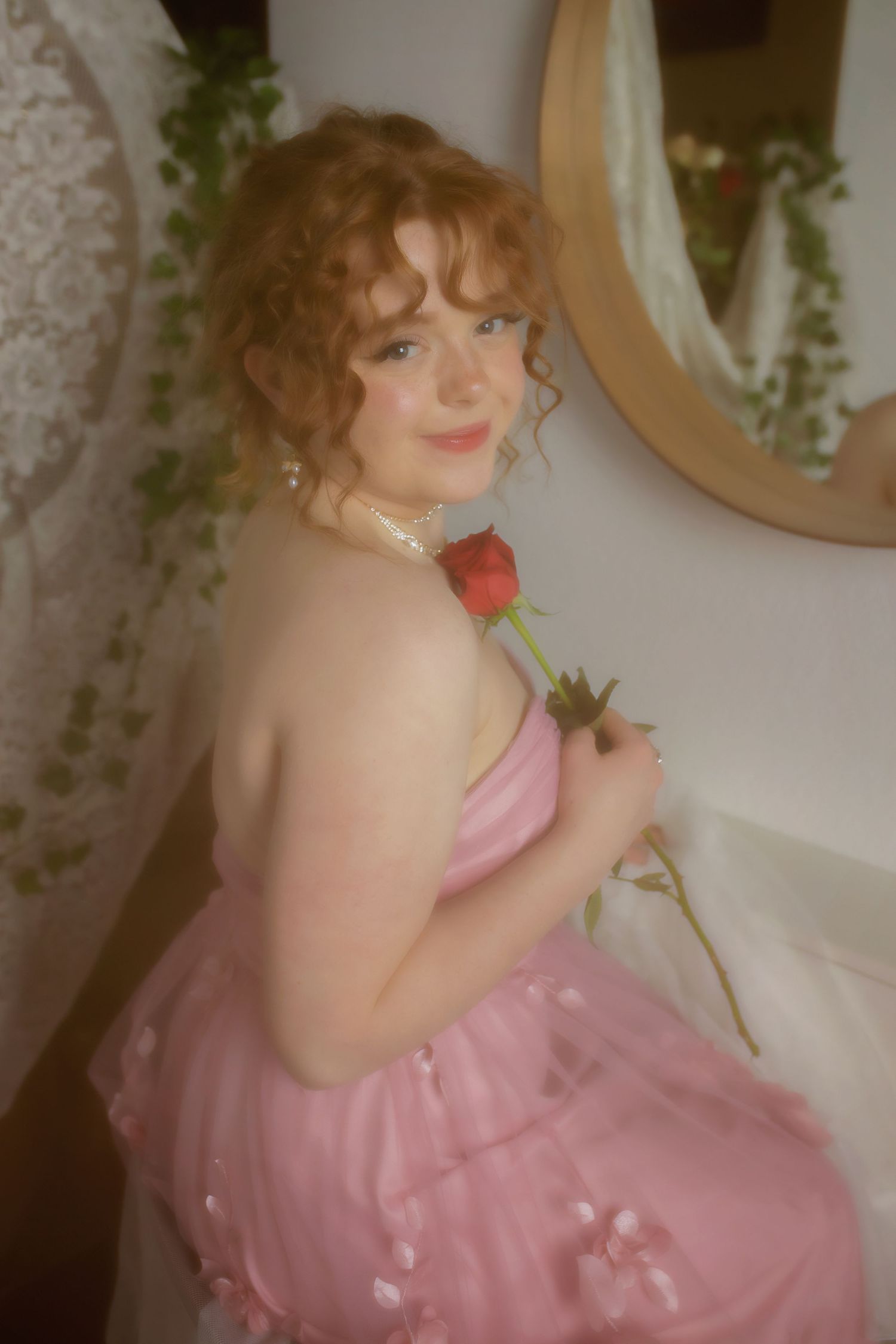 Colorado High School  woman in pink tulle dress holding a red rose, with curly auburn hair and pearl necklace, posing near a mirror Parker