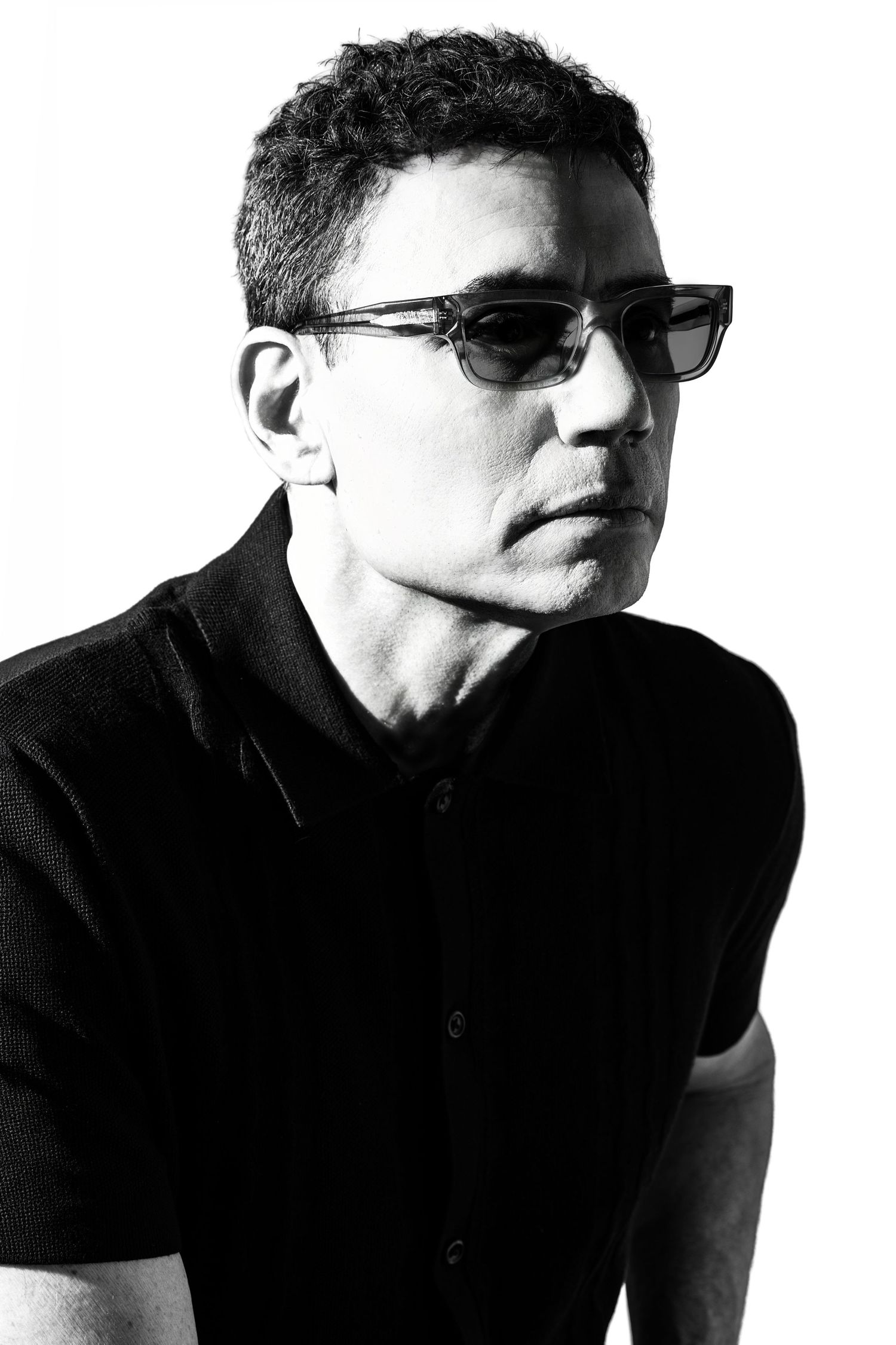 Moody black and white studio portrait of a man in a black polo shirt wearing sunglasses. Douglas Country Colorado Poet Headshot