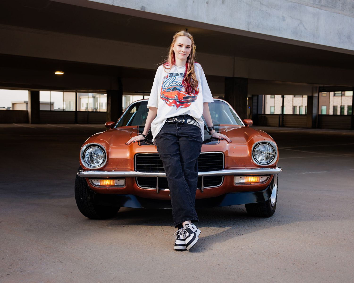 Young woman leaning against classic orange muscle car in parking garage Parker Denver CO Senior photos