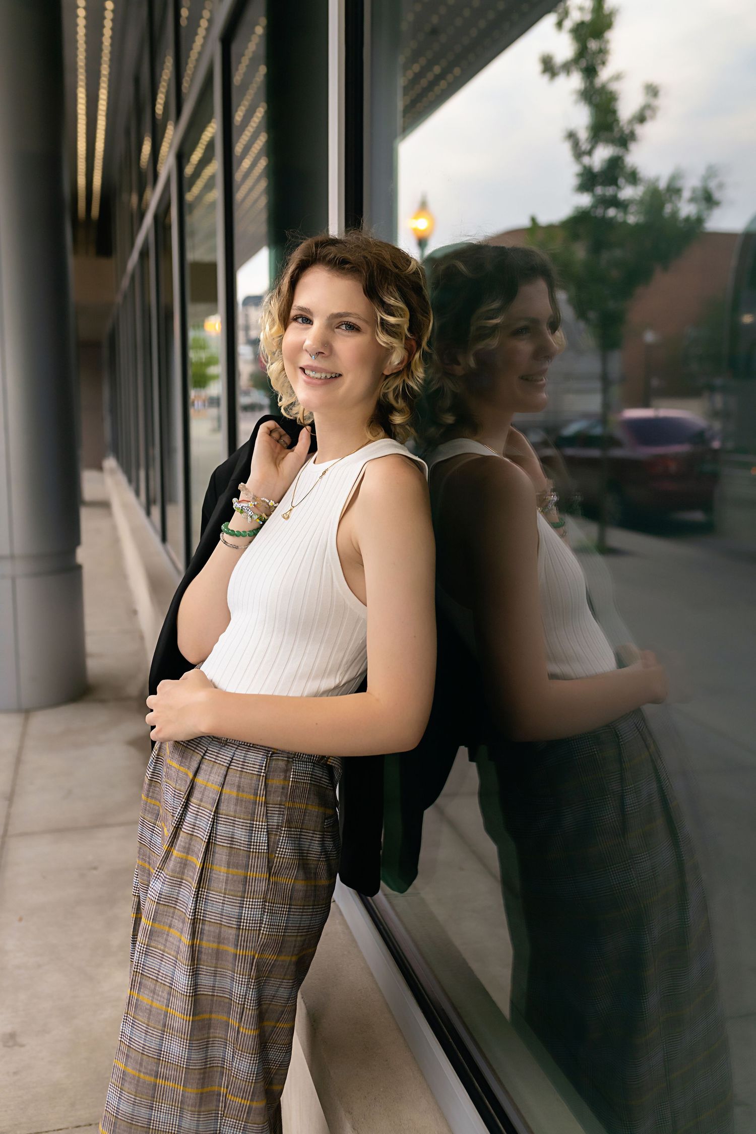 Teen in white ribbed tank and plaid pants leaning against glass window with reflection. Parker Colorado LGBTQ friendly images