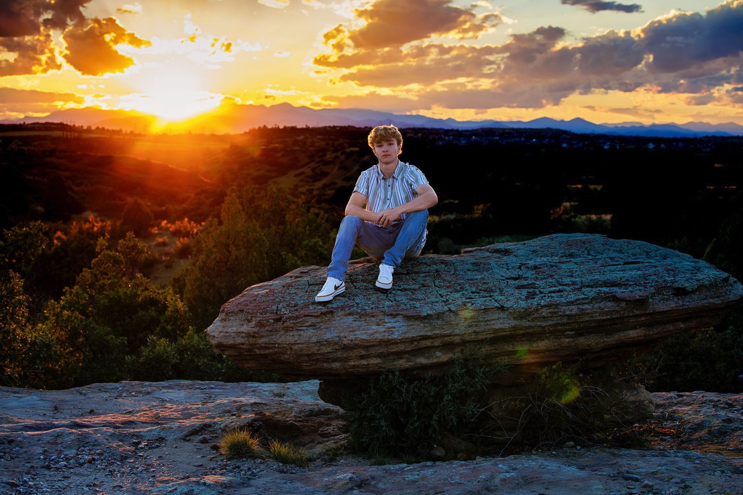 Teen boy sits on a flat rock at golden hour sunset with panoramic landscape views in the background.