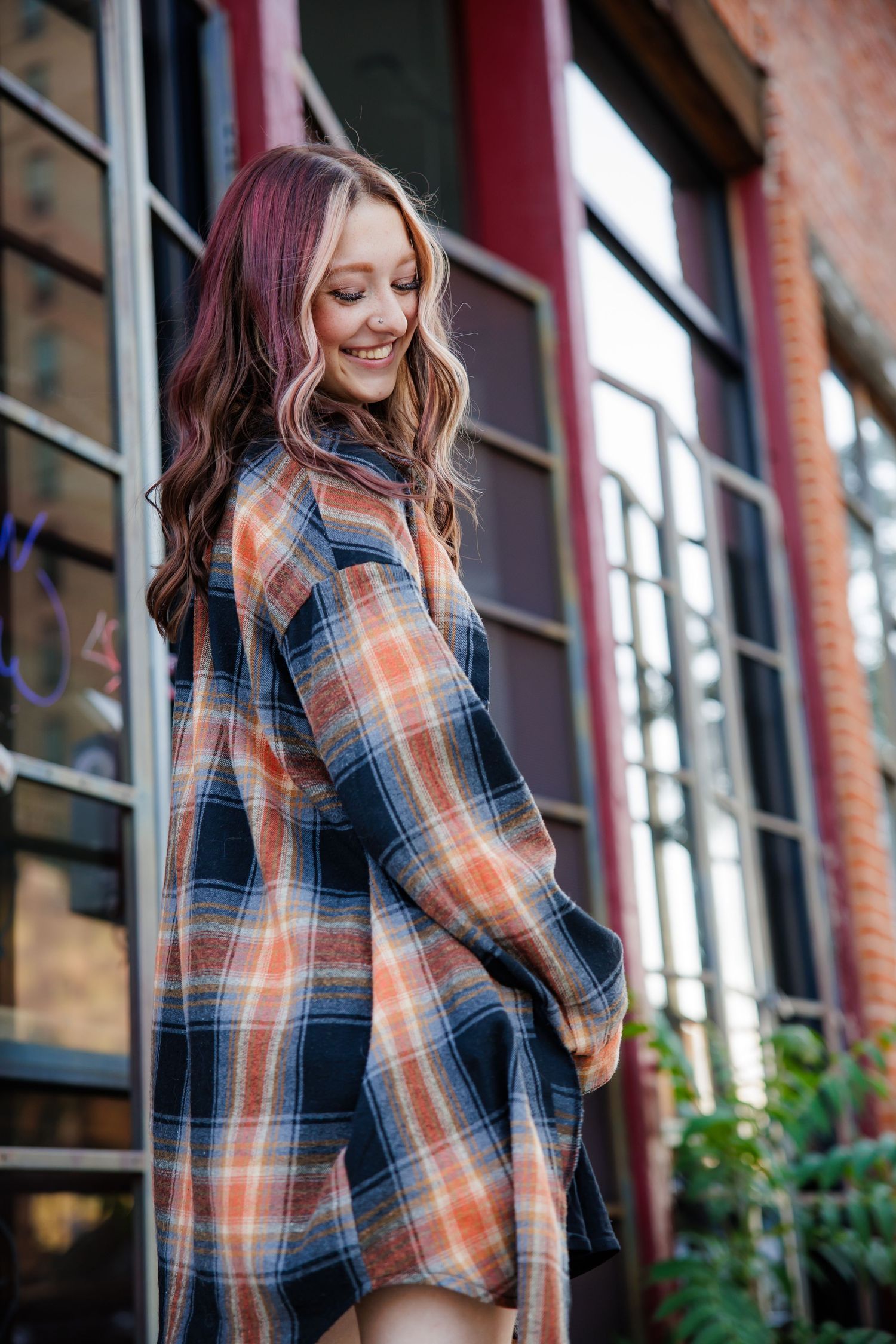 Smiling young woman in plaid flannel dress posing outdoors near brick building Downtown Denver CO Senior photos