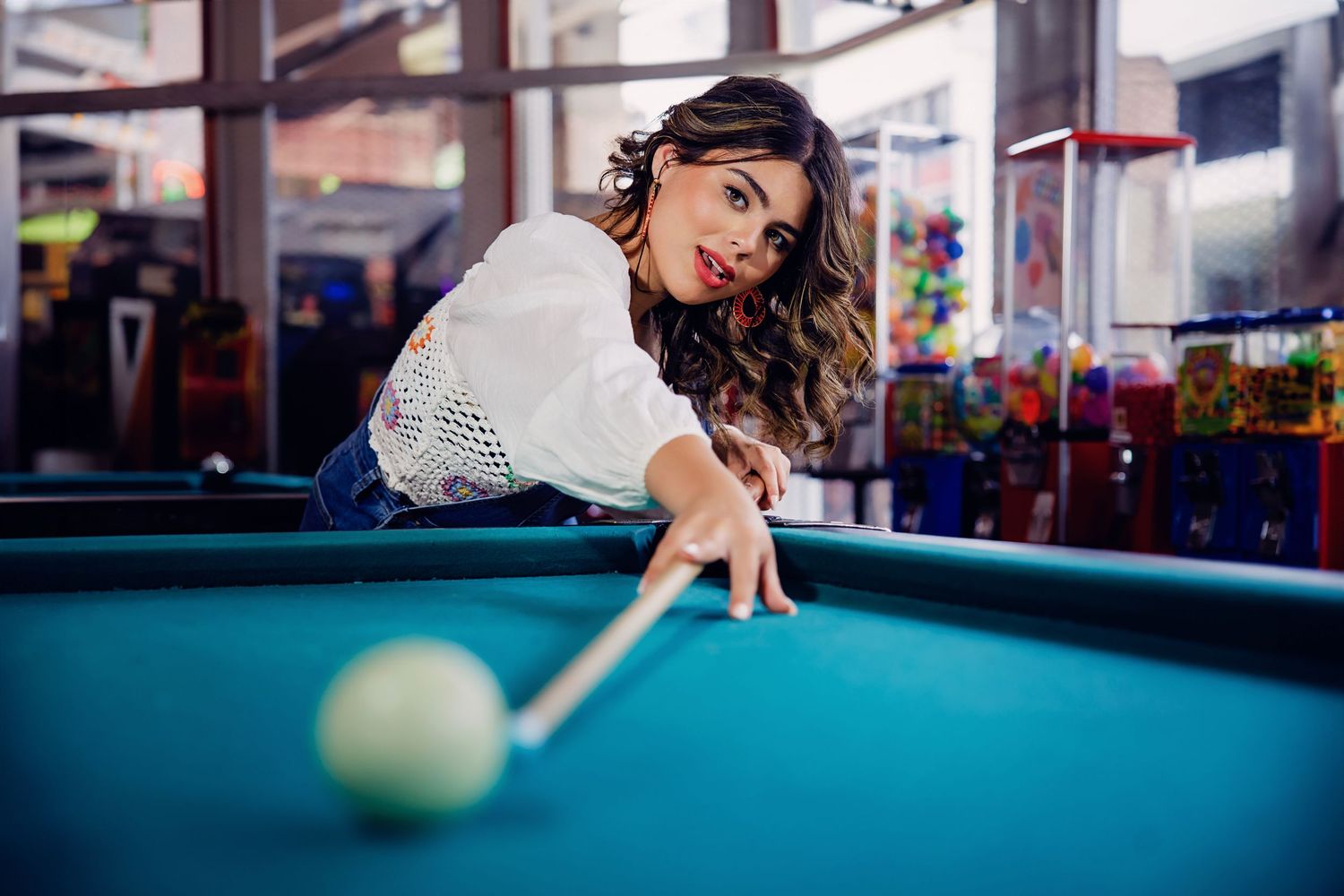 Young woman in white top leaning over pool table taking a billiards shot for Parker Colorado Senior pictures