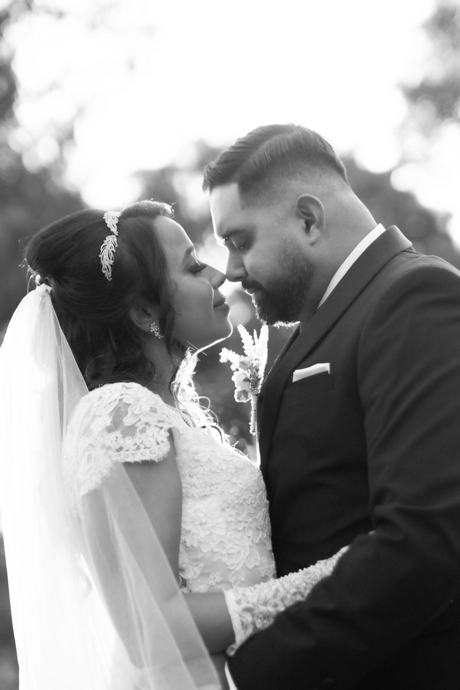 Black and white photo of a bride and groom sharing an intimate moment, nearly kissing, on their wedding day.