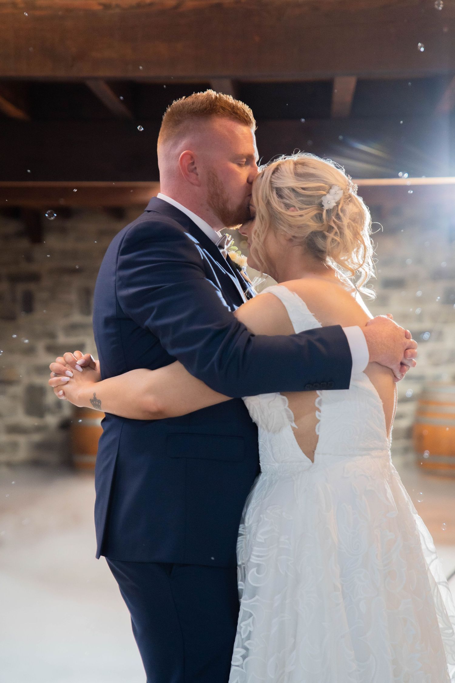 Newlyweds sharing their first dance kiss in a rustic stone barn venue with soft lighting.