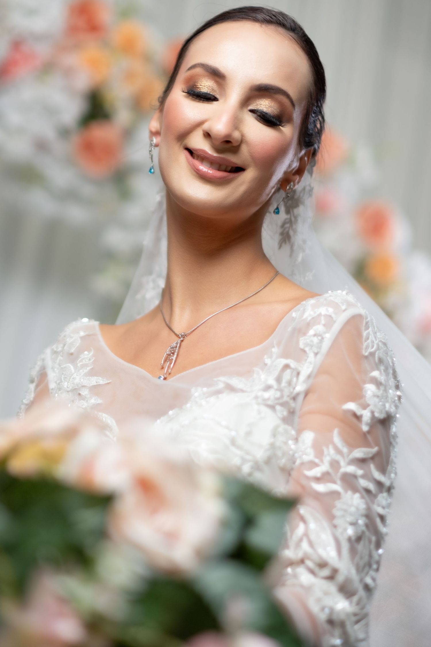 Joyful bride in lace gown with blue earrings and pendant necklace smiling.