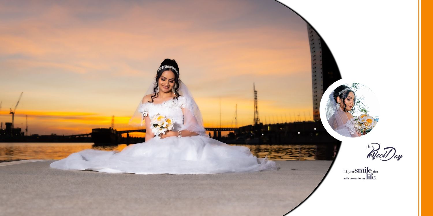 A bride in a full white gown poses at sunset near a waterfront with a city skyline in the background.