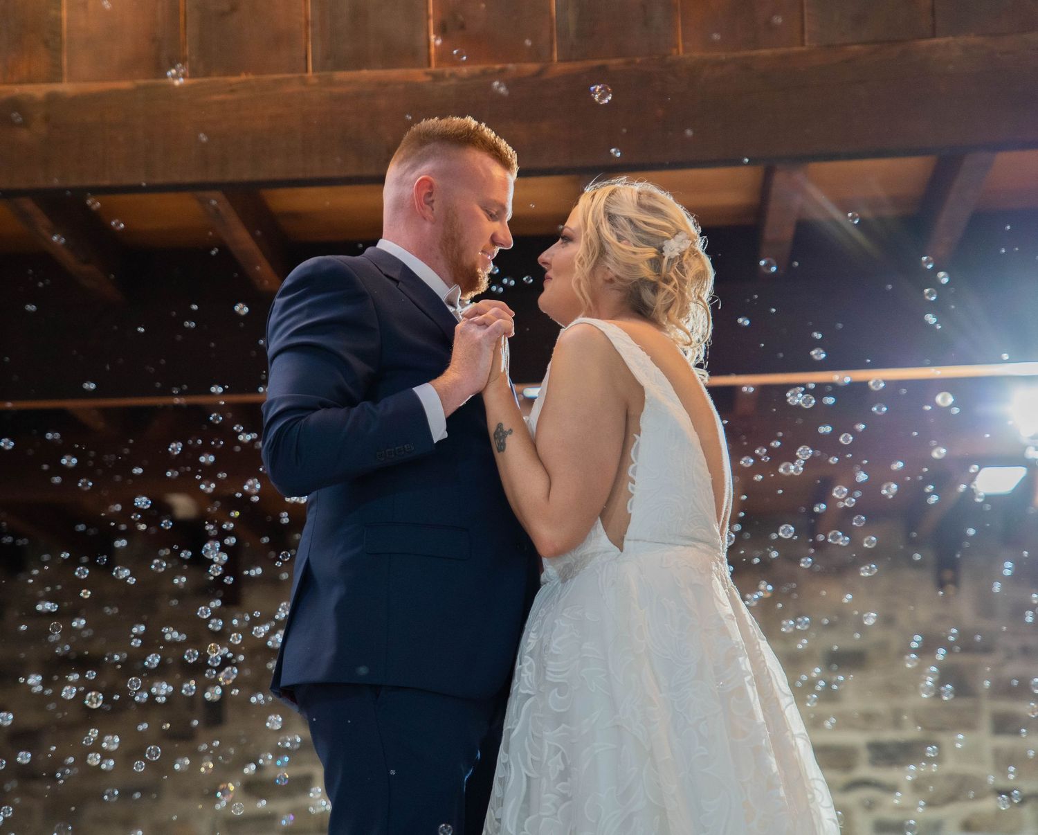 Bride and groom share an intimate moment surrounded by bubbles in a rustic barn wedding venue.