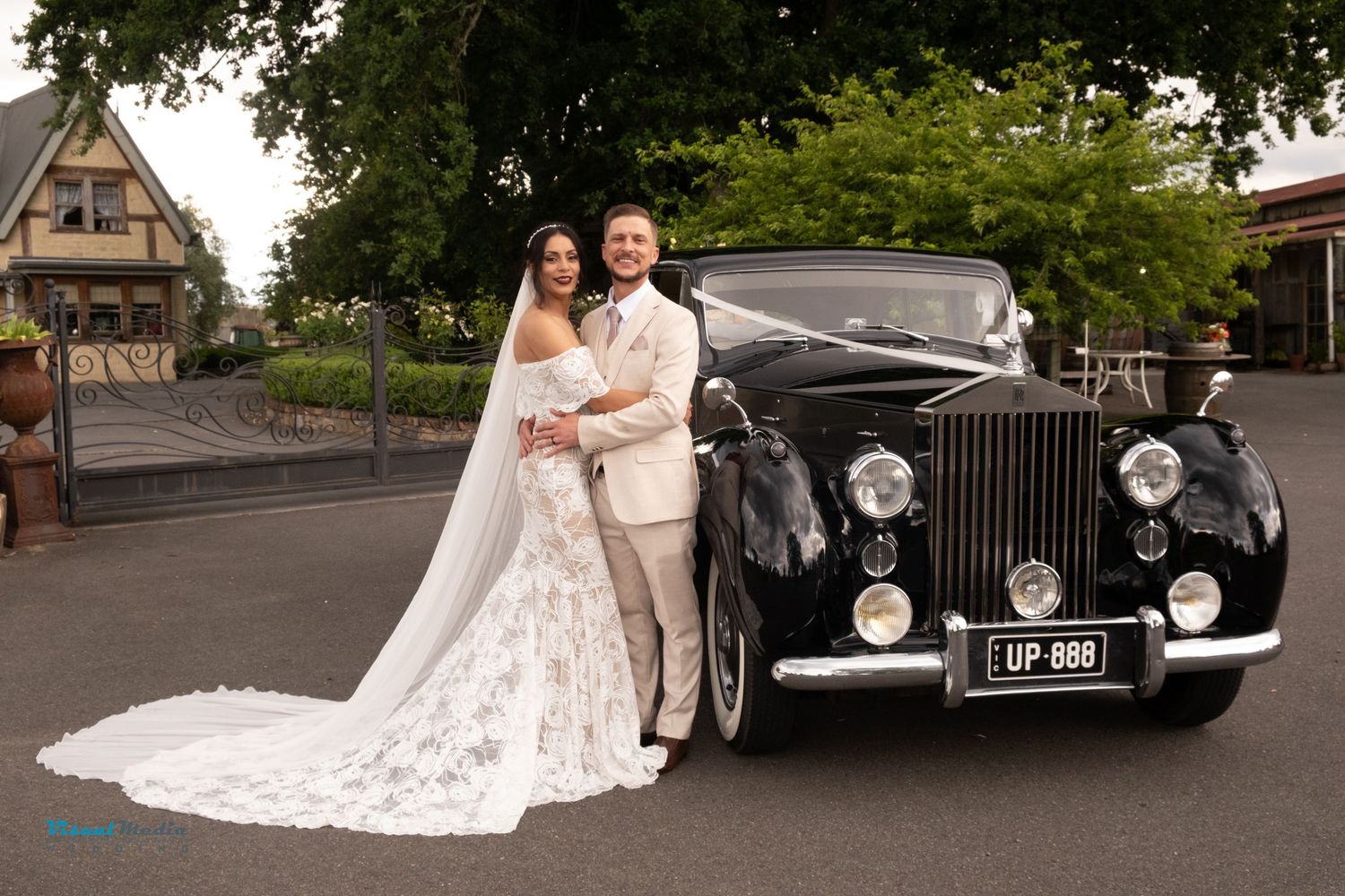 Wedding couple posing beside vintage black Rolls Royce car in elegant outdoor setting.