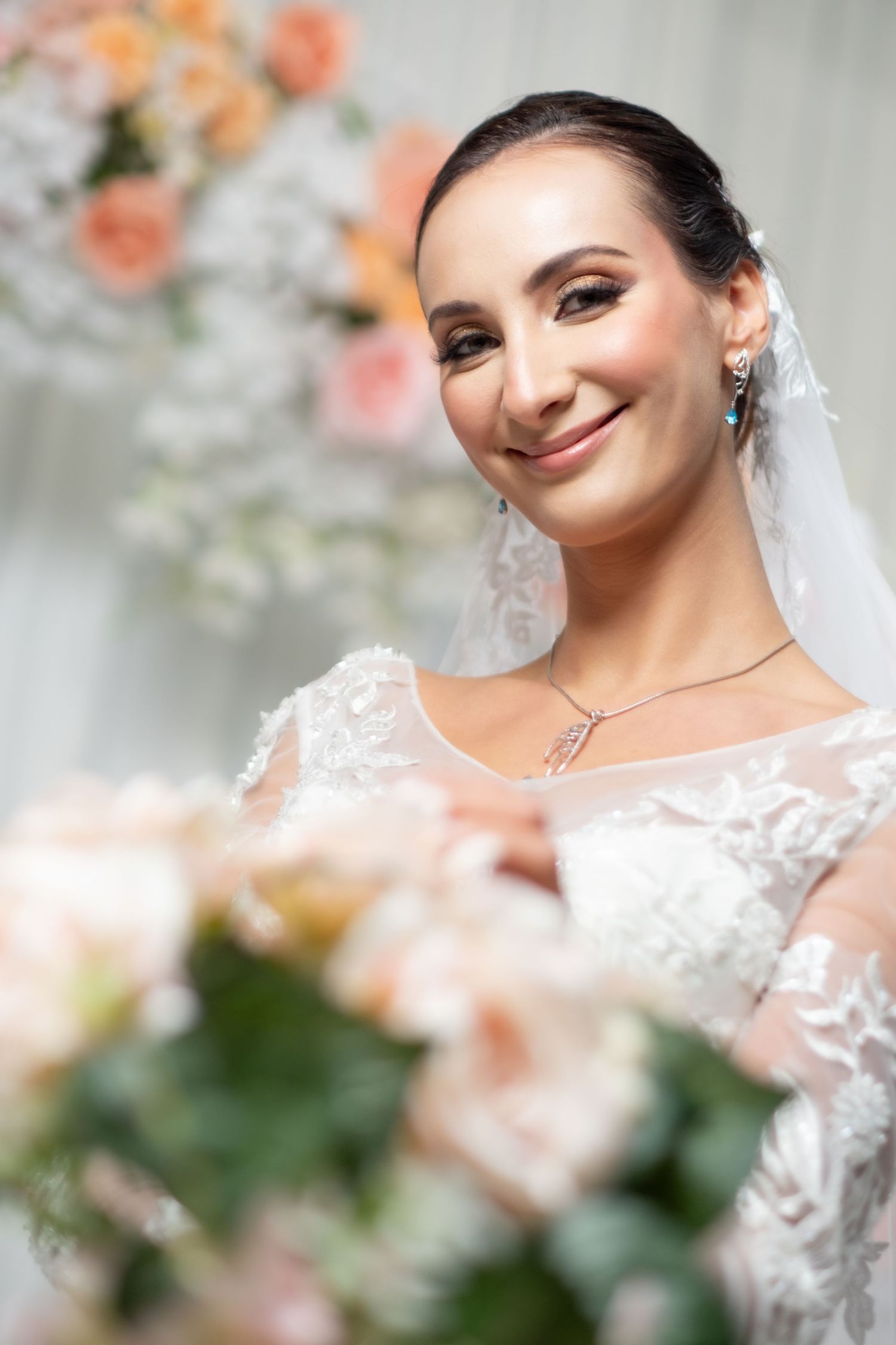 Smiling bride in lace wedding dress with teal earrings and diamond necklace.