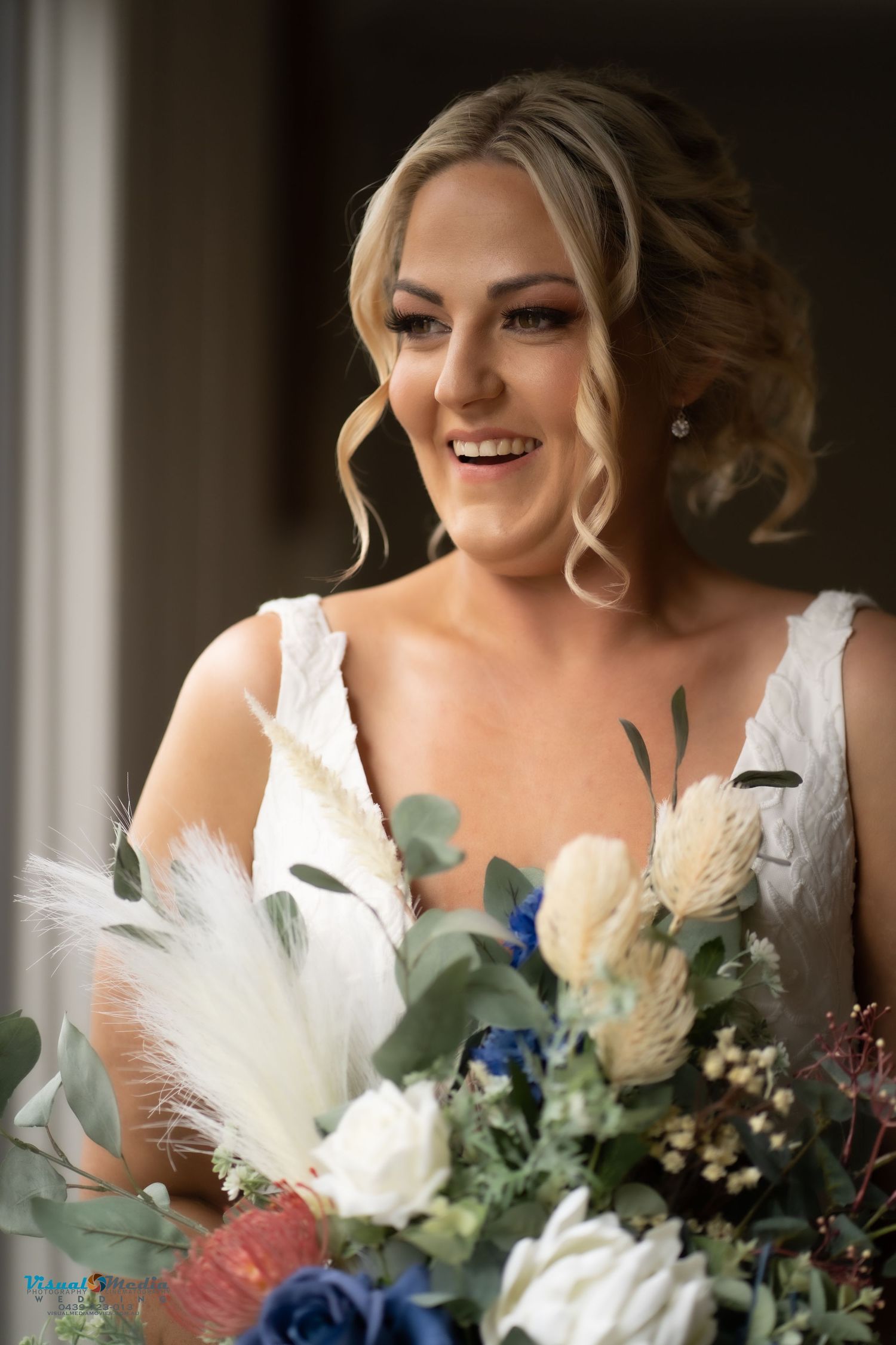 Radiant bride smiling while holding a stunning bouquet of white, blue, and neutral toned flowers.