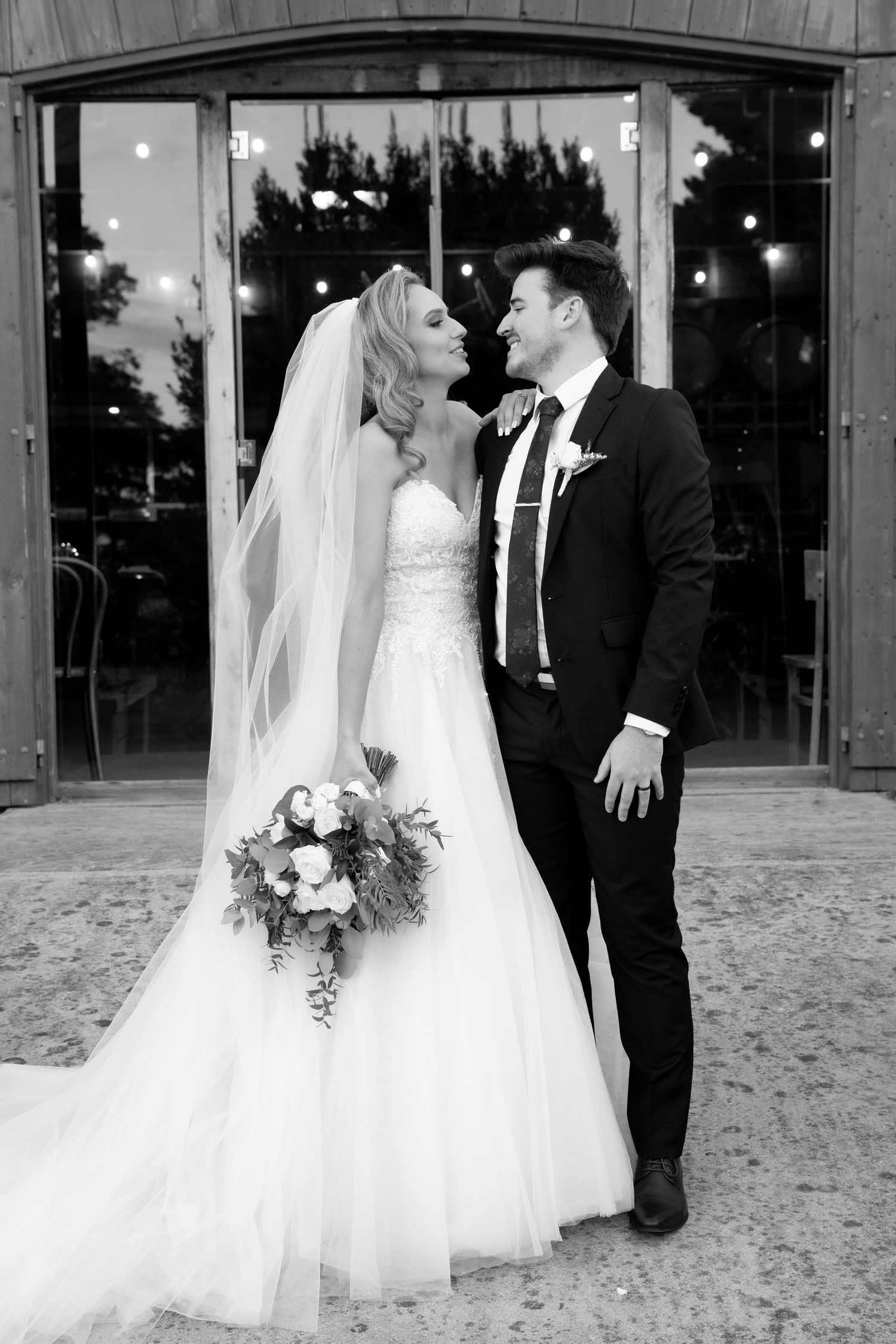 A bride and groom share a romantic moment outside in a black and white wedding photo.