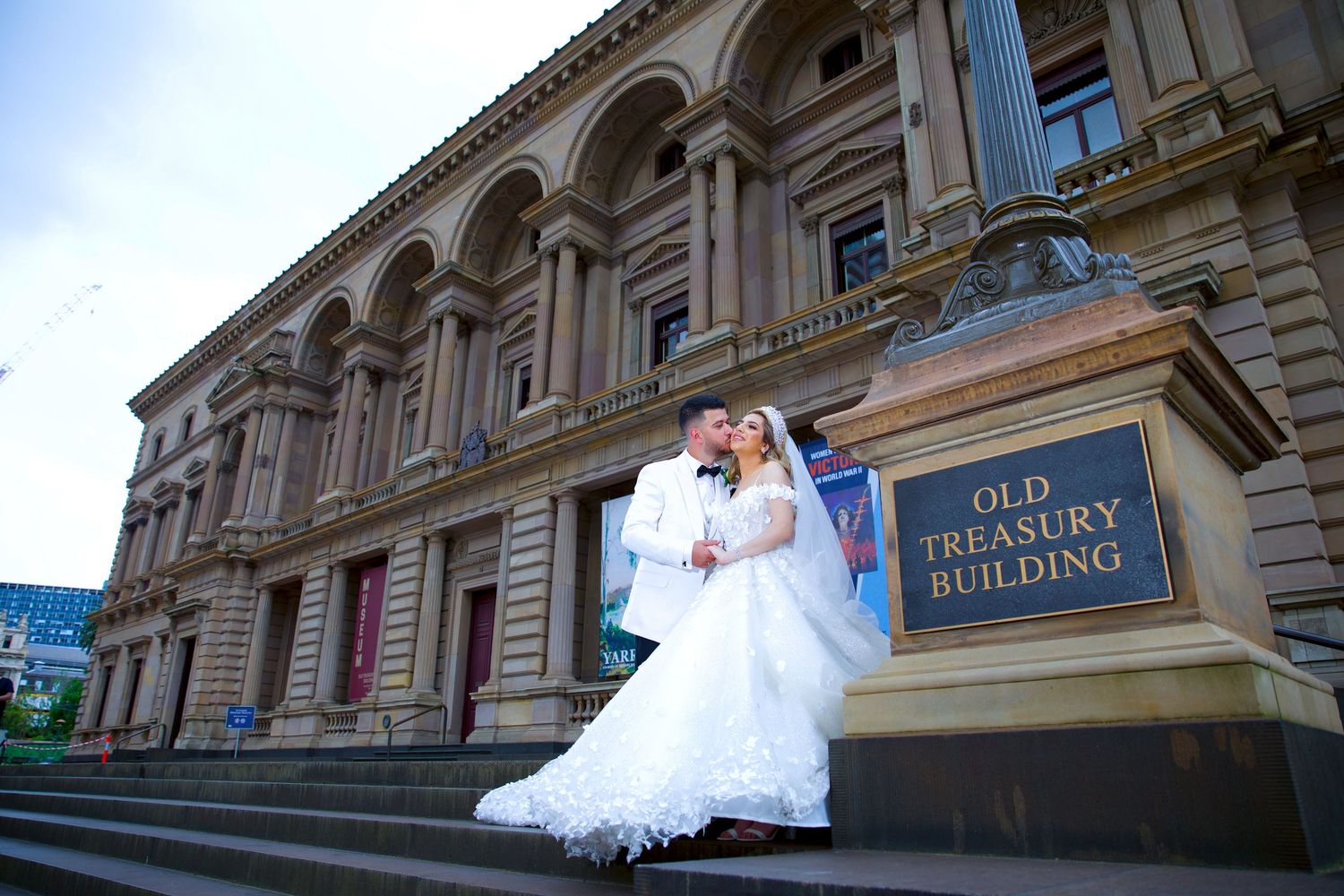 Bride and groom kissing on steps of historic Old Treasury Building on their wedding day.
