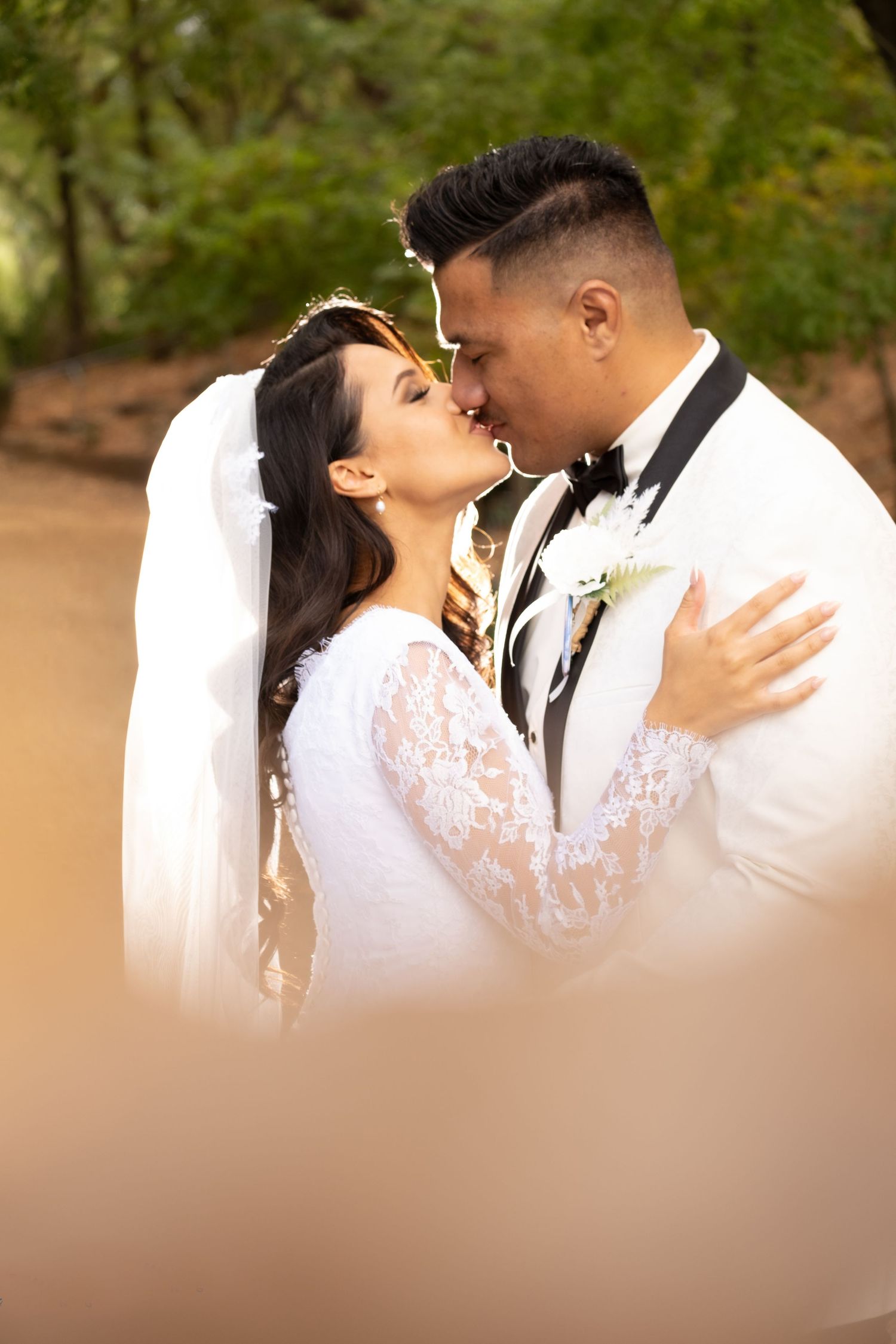 Bride and groom sharing a passionate kiss outdoors with a flowing white veil in nature.