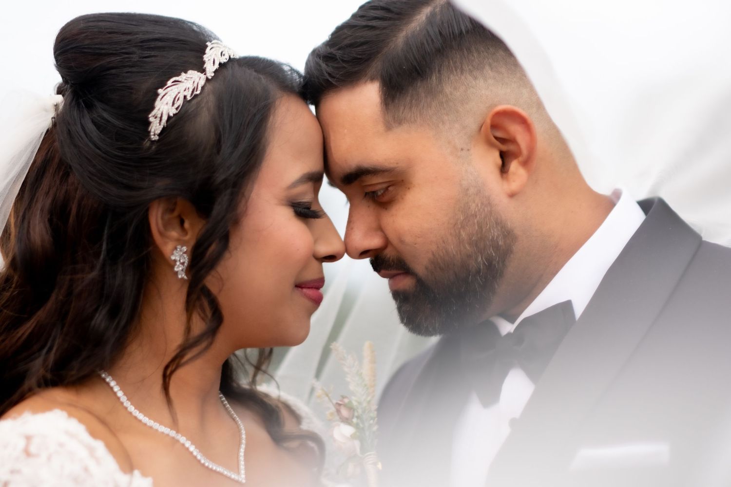 A bride and groom in wedding attire touch foreheads romantically, sharing an intimate moment on their wedding day.