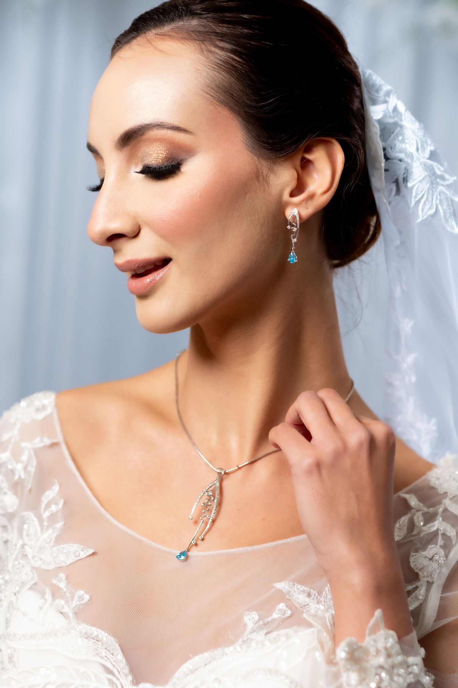 Elegant bride in lace gown wearing blue topaz earrings and delicate necklace.