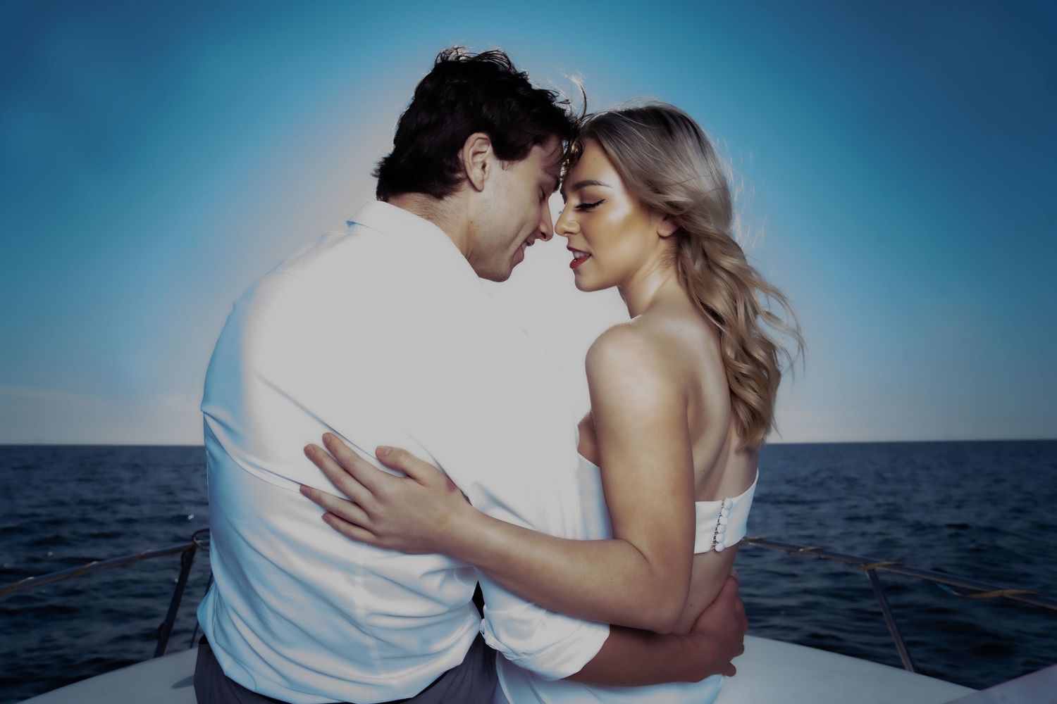 Romantic couple in wedding attire embracing closely on boat deck with ocean horizon behind.