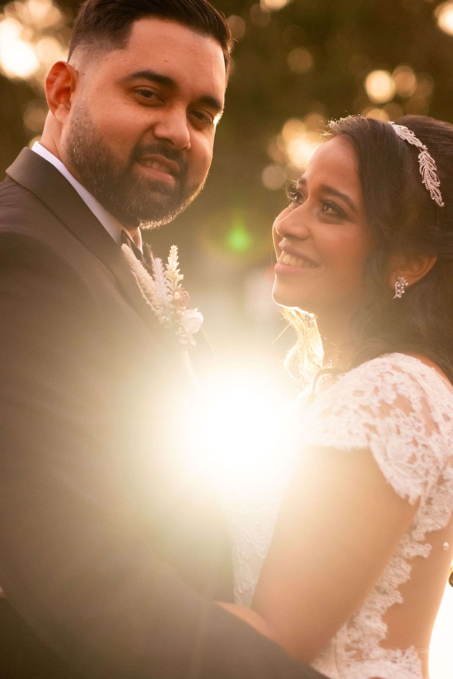 Bride smiling at groom in warm golden bokeh light wedding portrait.