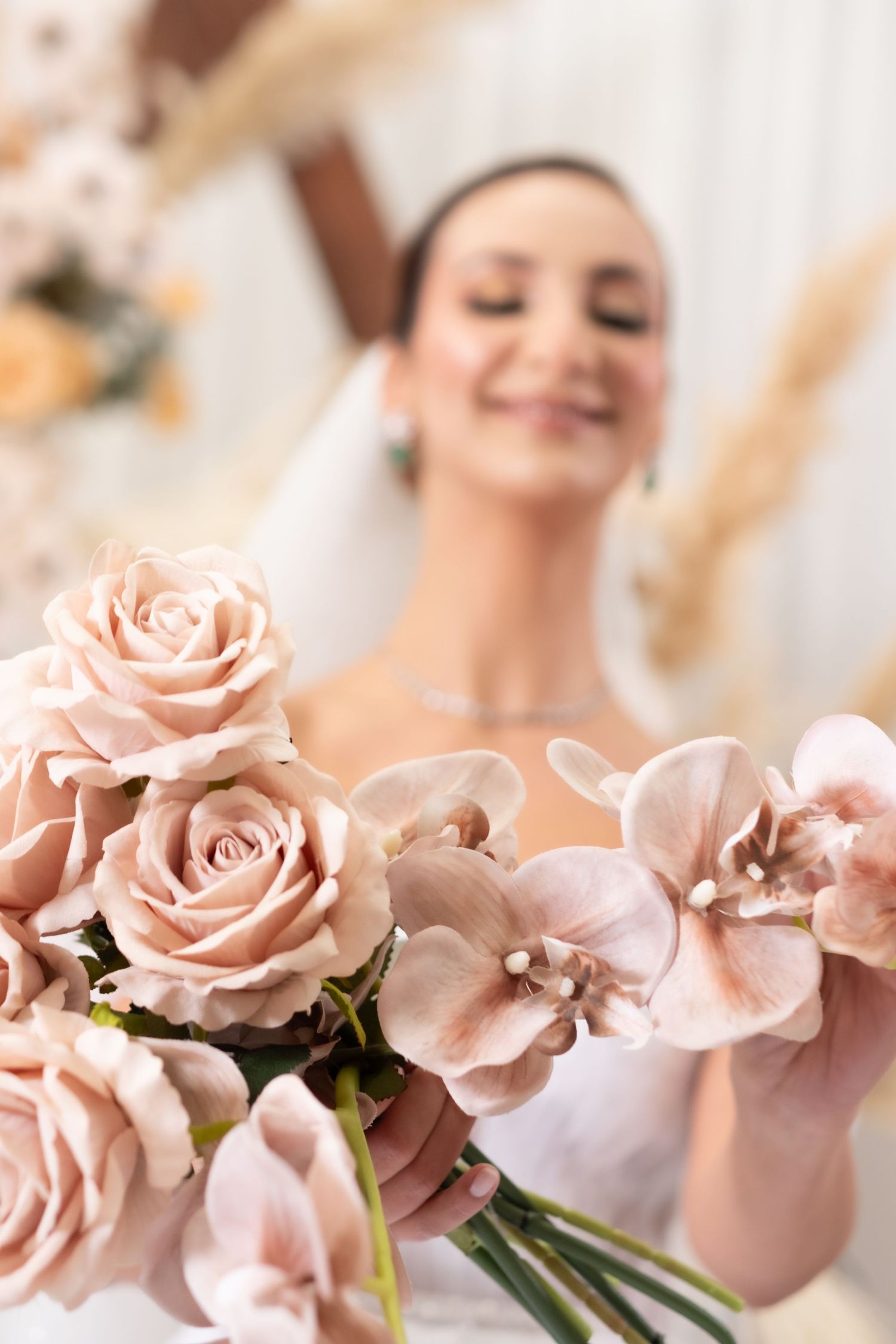 Close-up of blush pink roses and orchids bridal bouquet held by smiling bride in white wedding dress.