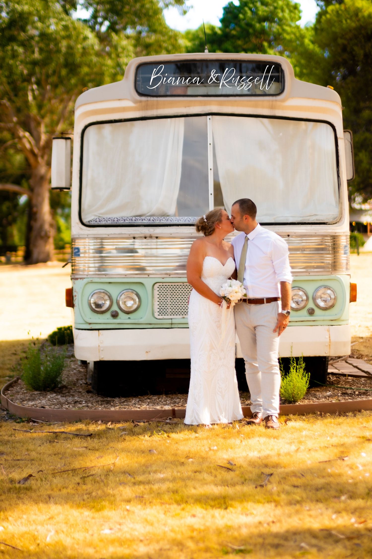 Bride and groom kissing in front of a vintage bus labeled Bianca and Russell outdoors.