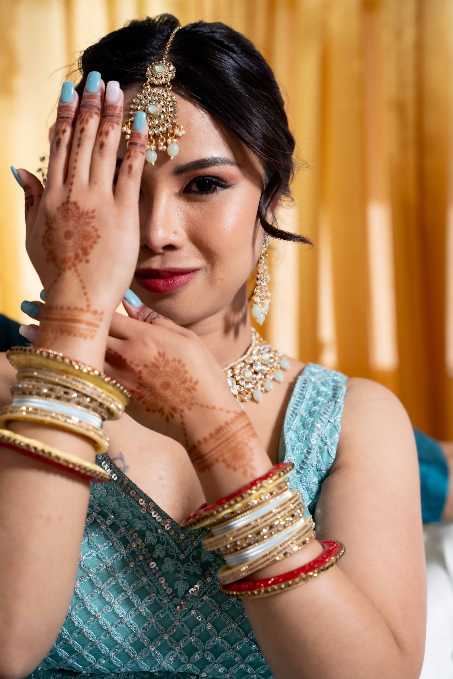 Indian bride showcasing intricate henna designs and gold bangles in traditional bridal attire.