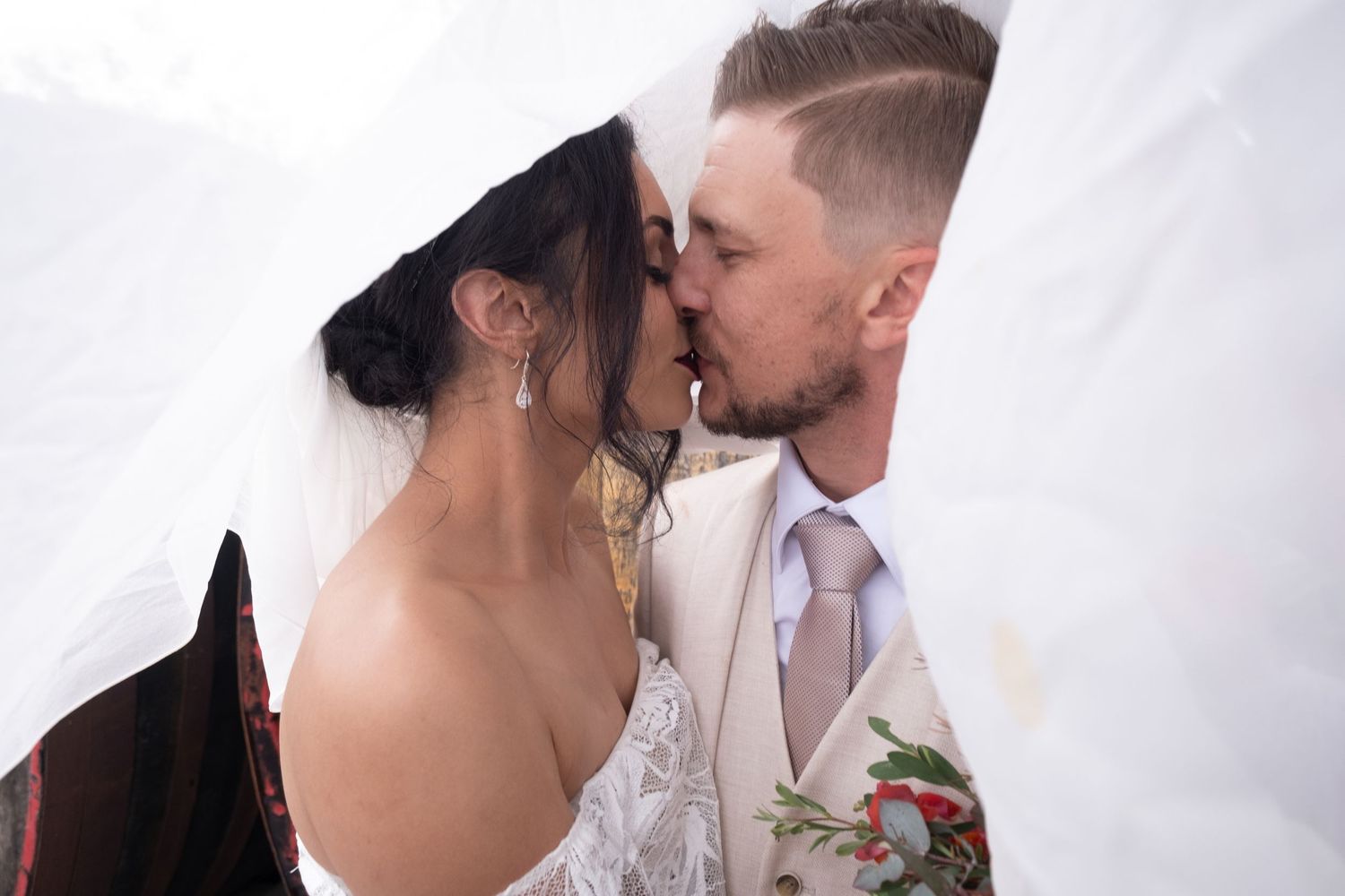 Bride and groom sharing an intimate kiss hidden beneath the bride's flowing white wedding veil.