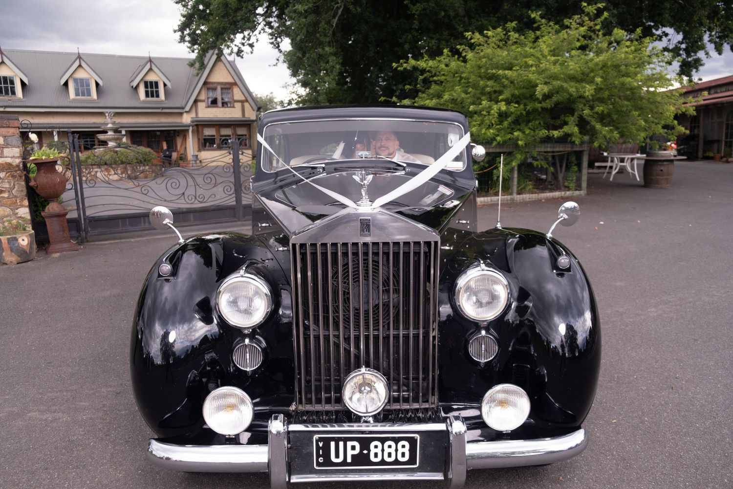 Classic black Rolls-Royce wedding car with white ribbon decoration and UP 888 license plate parked outside venue.