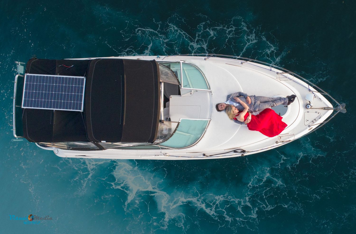 Aerial view of couple relaxing on white motorboat with solar panel on blue water.